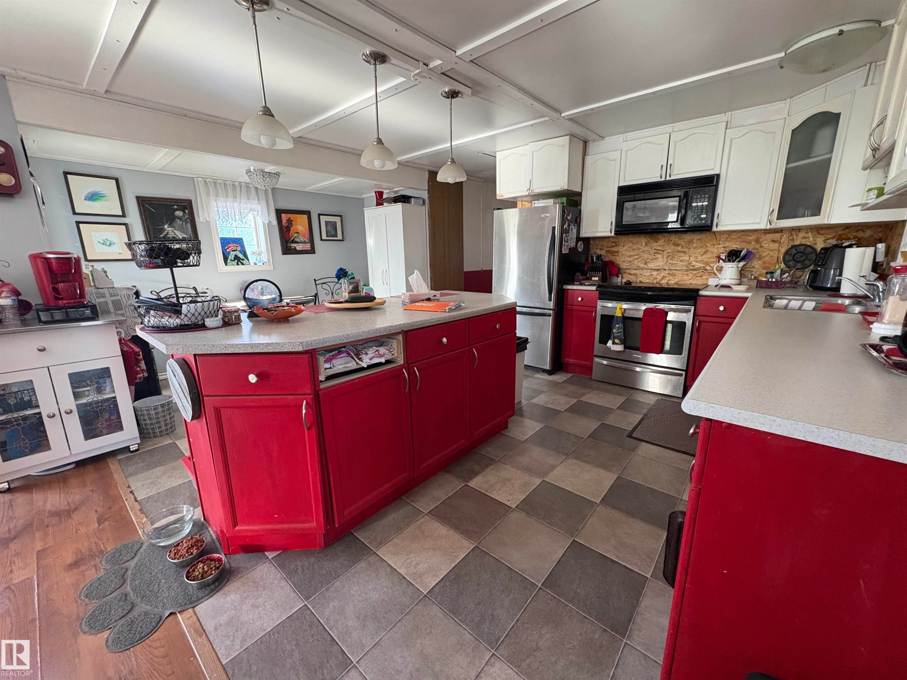 Spacious kitchen featuring a large central island with bright red cabinetry, white upper cabinetry, and a stainless steel appliance suite including a refrigerator, range, and microwave. - 115 2Nd Street E, Derwent, AB - Indoor Photo Showing Kitchen With Double Sink