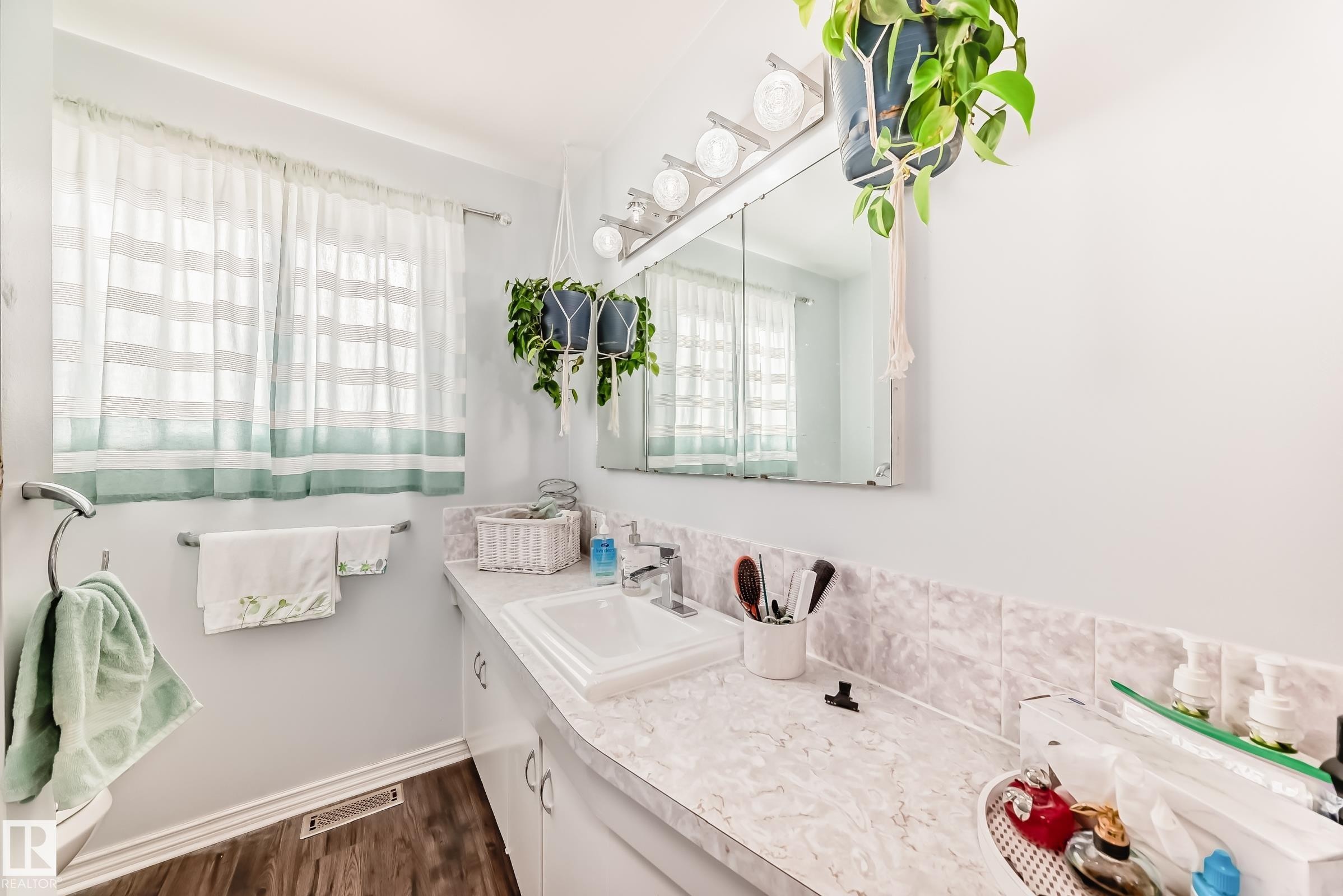 Bathroom featuring a vanity with an integrated sink, a wall-mounted mirror, overhead vanity lighting, and wood-finish flooring - 3611 108 Street, Edmonton, AB - Indoor Photo Showing Bathroom