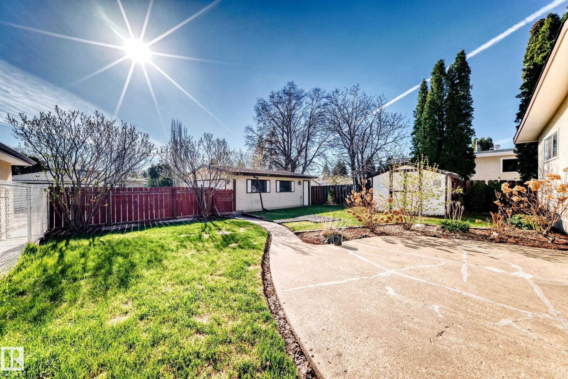 Expansive backyard featuring a curved concrete walkway, a manicured lawn, perimeter fencing, and mature landscaping - 3611 108 Street, Edmonton, AB - Outdoor