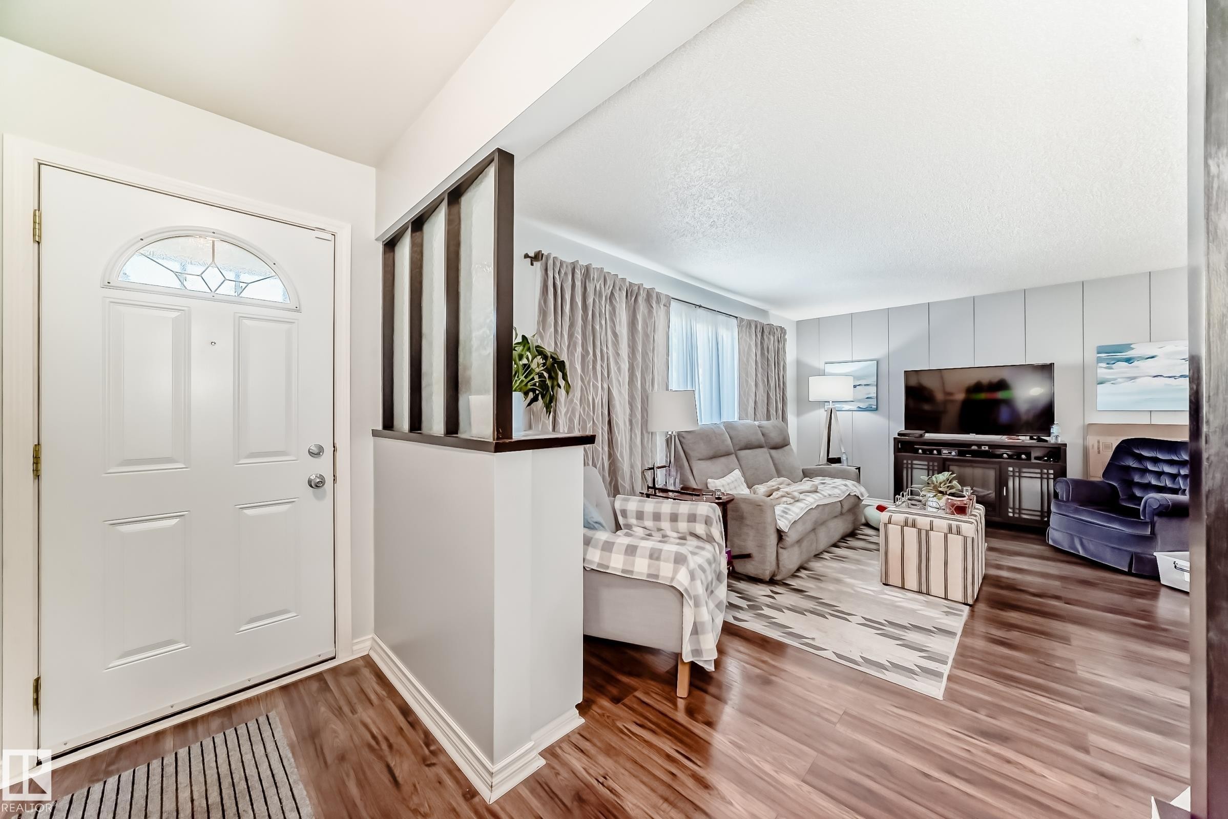 Entryway with a paneled white door featuring an arched decorative glass insert and complementing wood-finish flooring - 3611 108 Street, Edmonton, AB - Indoor