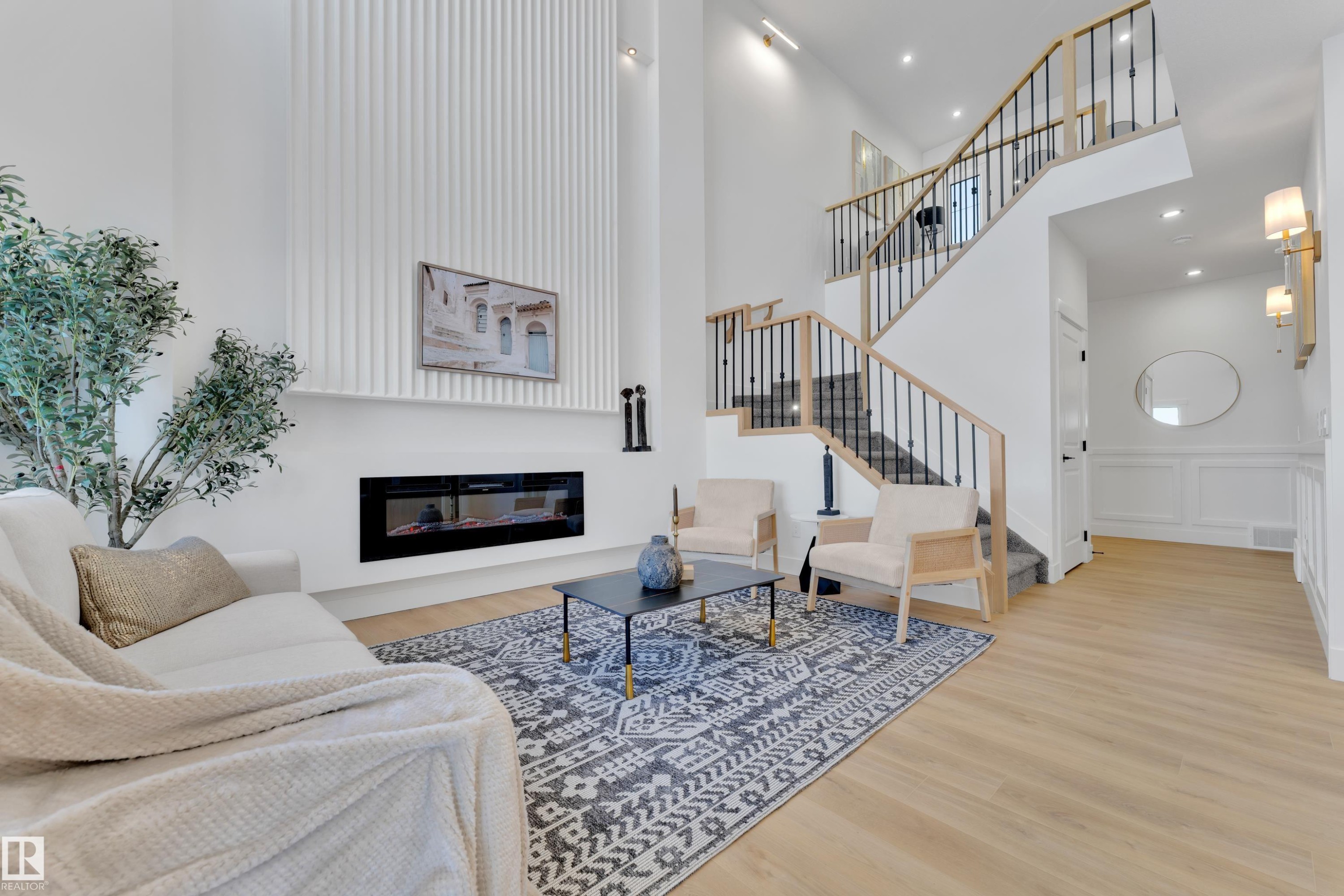 Two-story living area featuring a prominent linear fireplace, vertical wall paneling, light wood-finish flooring, and a multi-level staircase with open risers and wrought iron balusters - 382 Linden Loop, Leduc, AB - Indoor Photo Showing Other Room With Fireplace