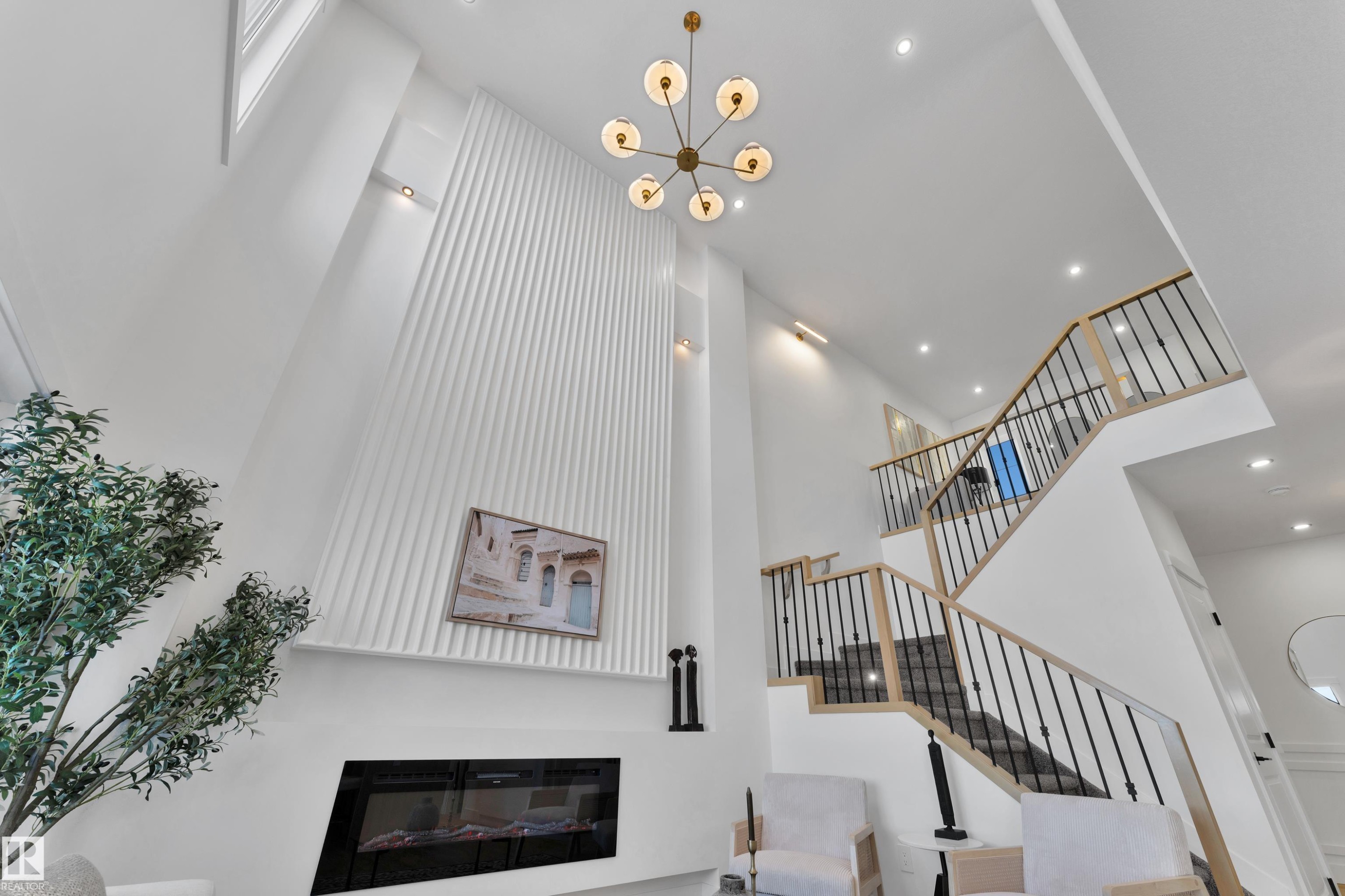 Two-story interior with a modern chandelier, recessed lighting, and a prominent staircase featuring wood-finish handrails and black metal spindles - 382 Linden Loop, Leduc, AB - Indoor Photo Showing Other Room With Fireplace