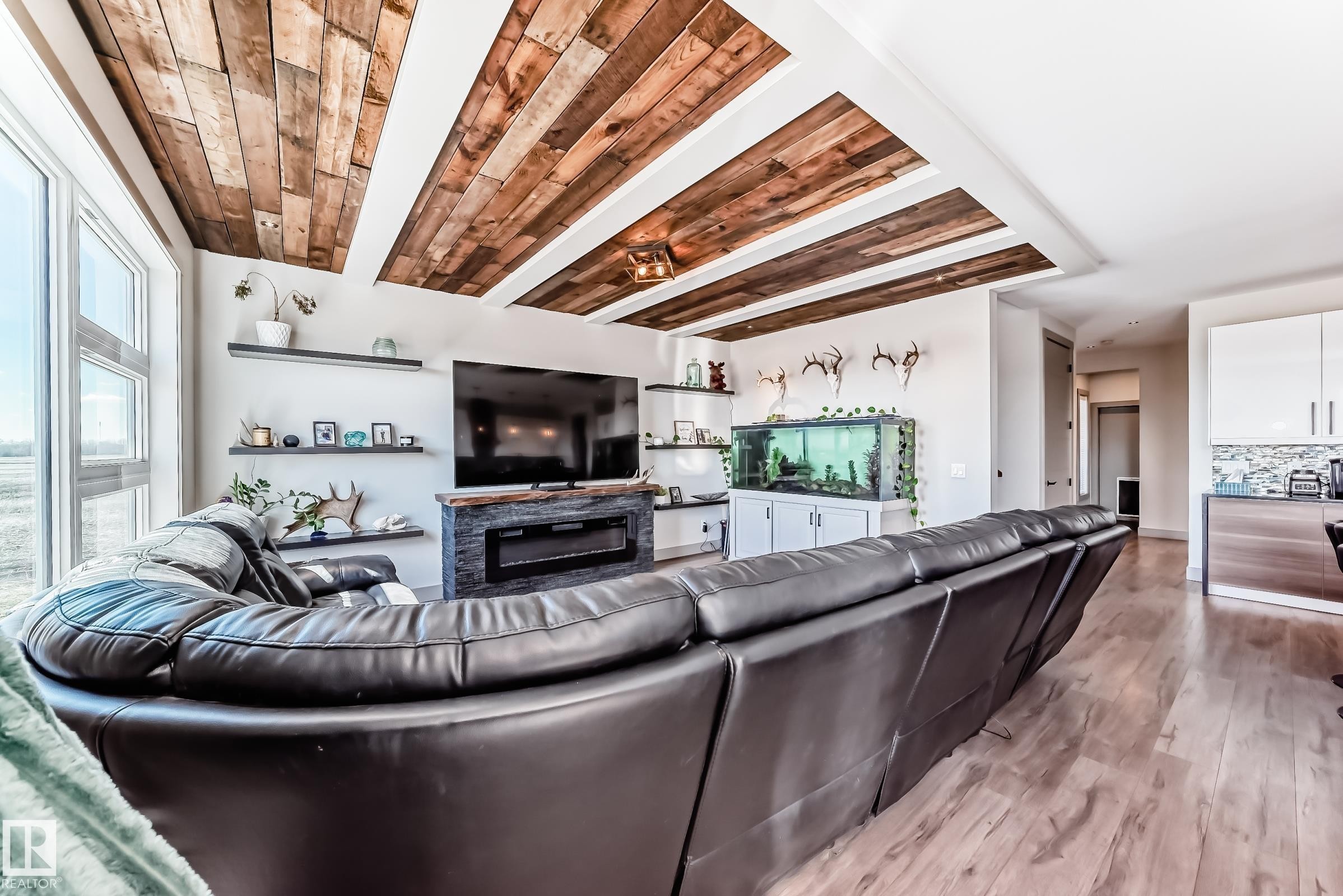 Vaulted ceiling with wood-panel accents, large picture windows, wood-finish flooring, built-in shelving, and an electric fireplace feature - 5263 47 Ave, Calmar, AB - Indoor With Fireplace