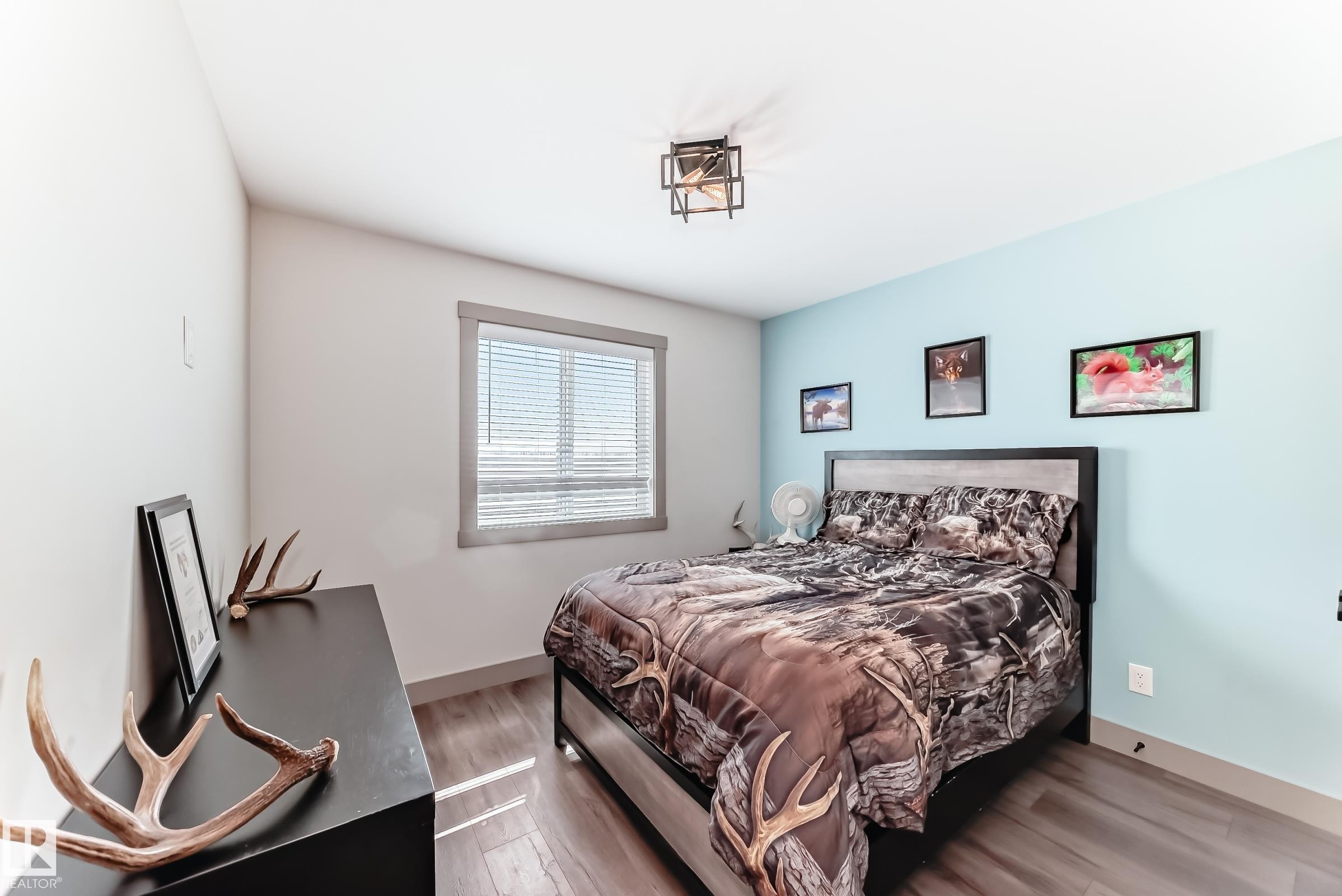 Bedroom featuring wood-finish flooring, a contemporary ceiling light fixture, a window with horizontal blinds, and a two-tone accent wall - 5263 47 Ave, Calmar, AB - Indoor Photo Showing Bedroom