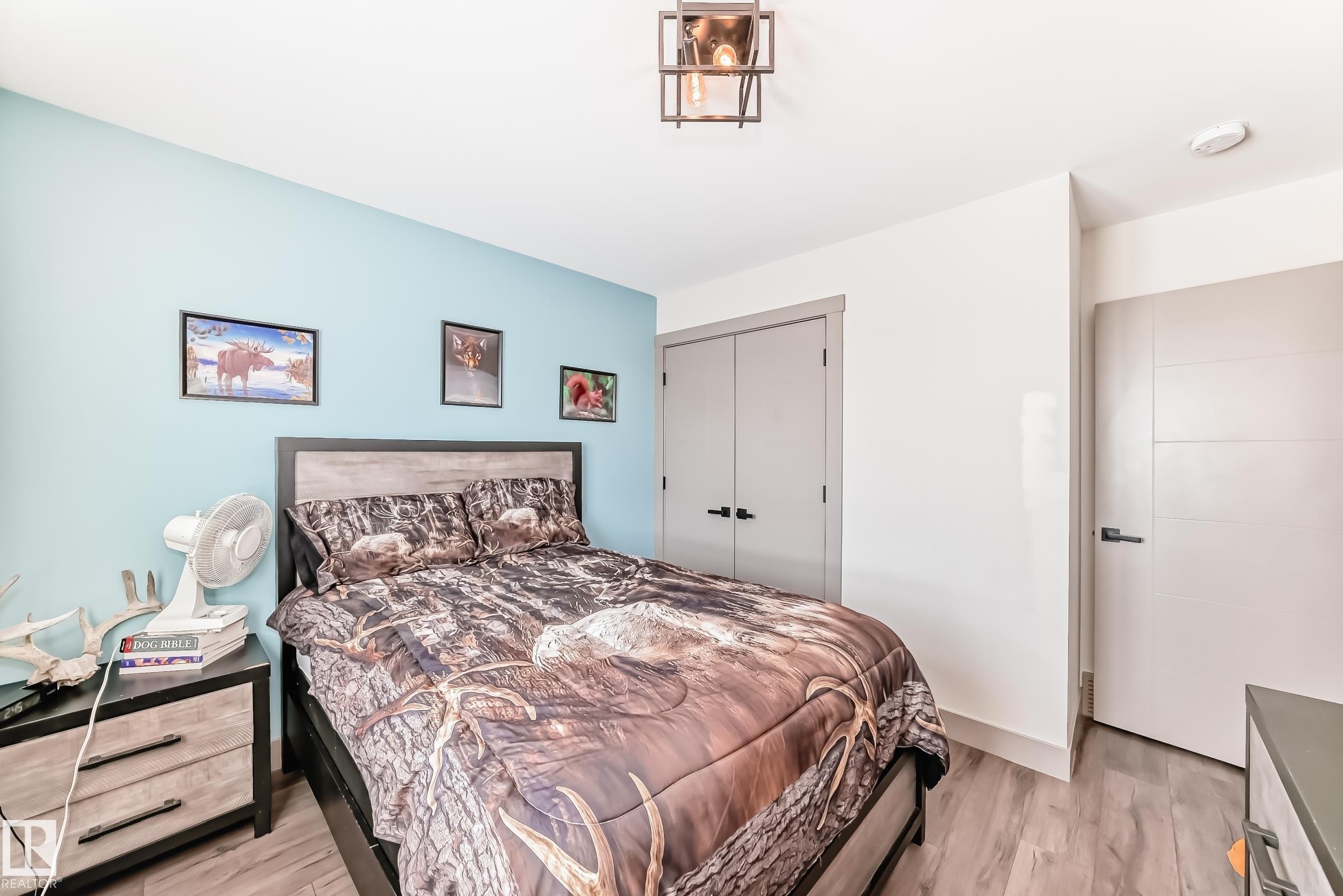Bedroom featuring wood-finish flooring, a light blue accent wall, modern ceiling light fixture, and two panel doors - 5263 47 Ave, Calmar, AB - Indoor Photo Showing Bedroom