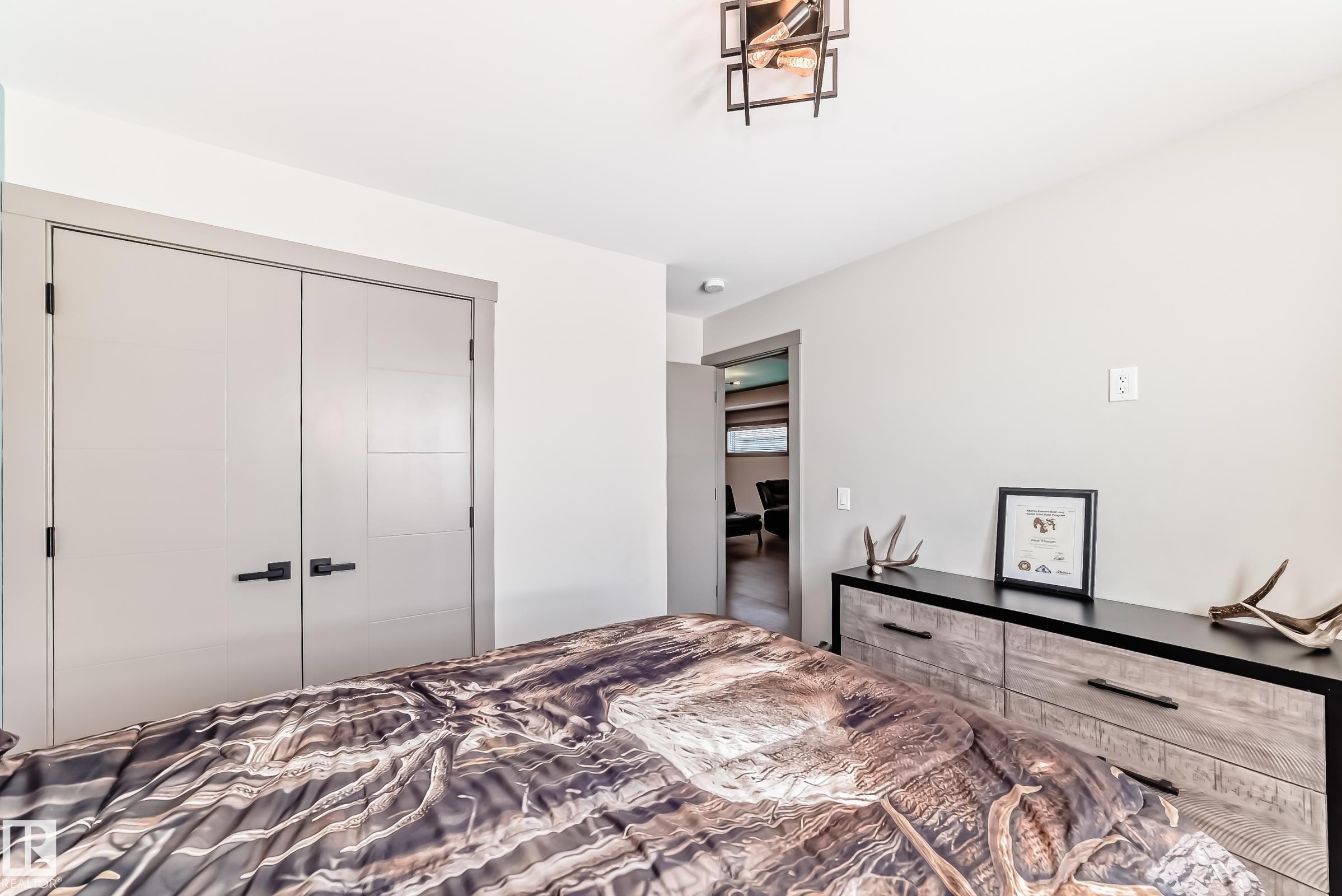 Bedroom featuring a contemporary ceiling light fixture, light gray walls, and light gray double closet doors with black hardware - 5263 47 Ave, Calmar, AB - Indoor Photo Showing Bedroom