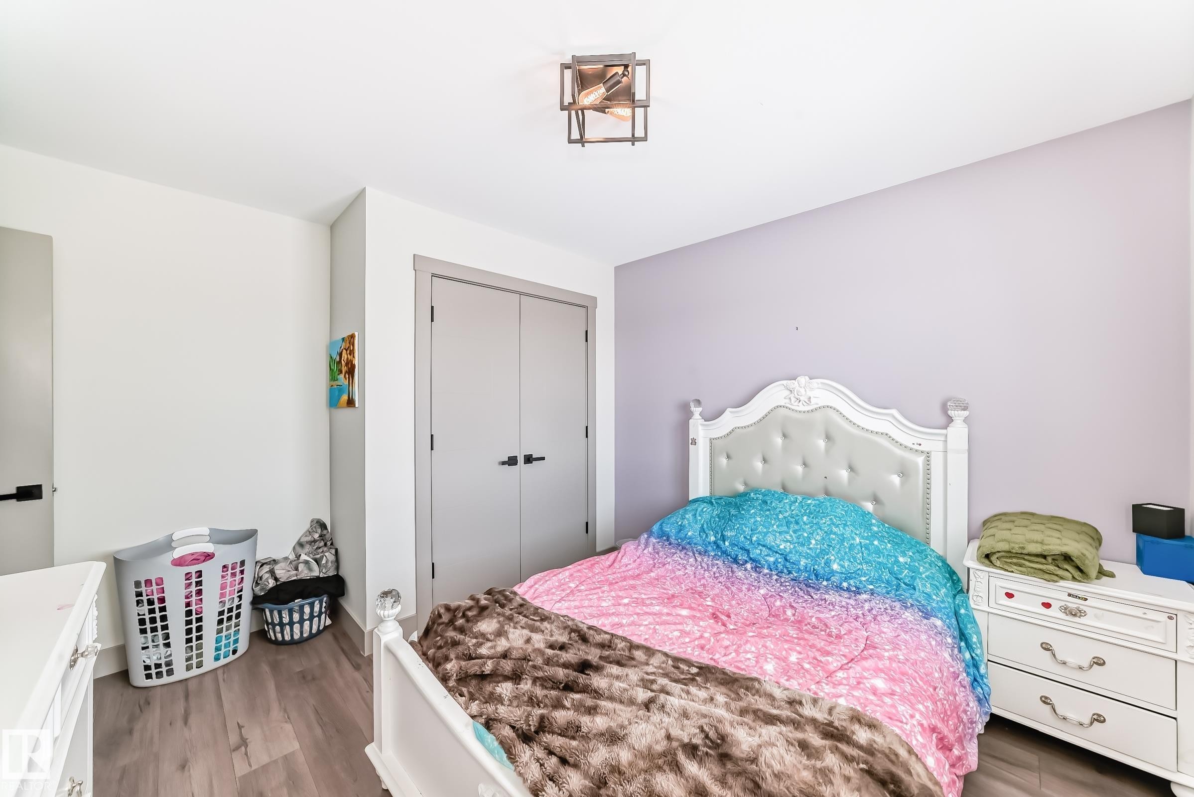 Spacious bedroom featuring wood-finish flooring, a contemporary ceiling light fixture, and a neutral color palette with an accent wall - 5263 47 Ave, Calmar, AB - Indoor Photo Showing Bedroom
