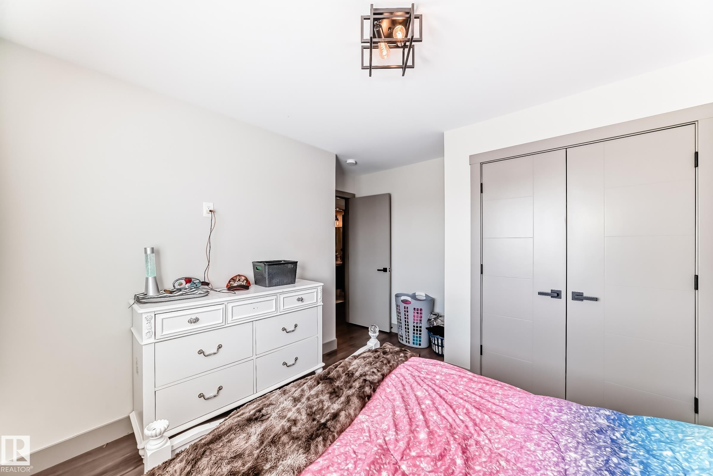 Contemporary flush-panel closet doors with matte black hardware, wood-finish flooring, and a modern geometric flush-mount ceiling light fixture - 5263 47 Ave, Calmar, AB - Indoor Photo Showing Bedroom