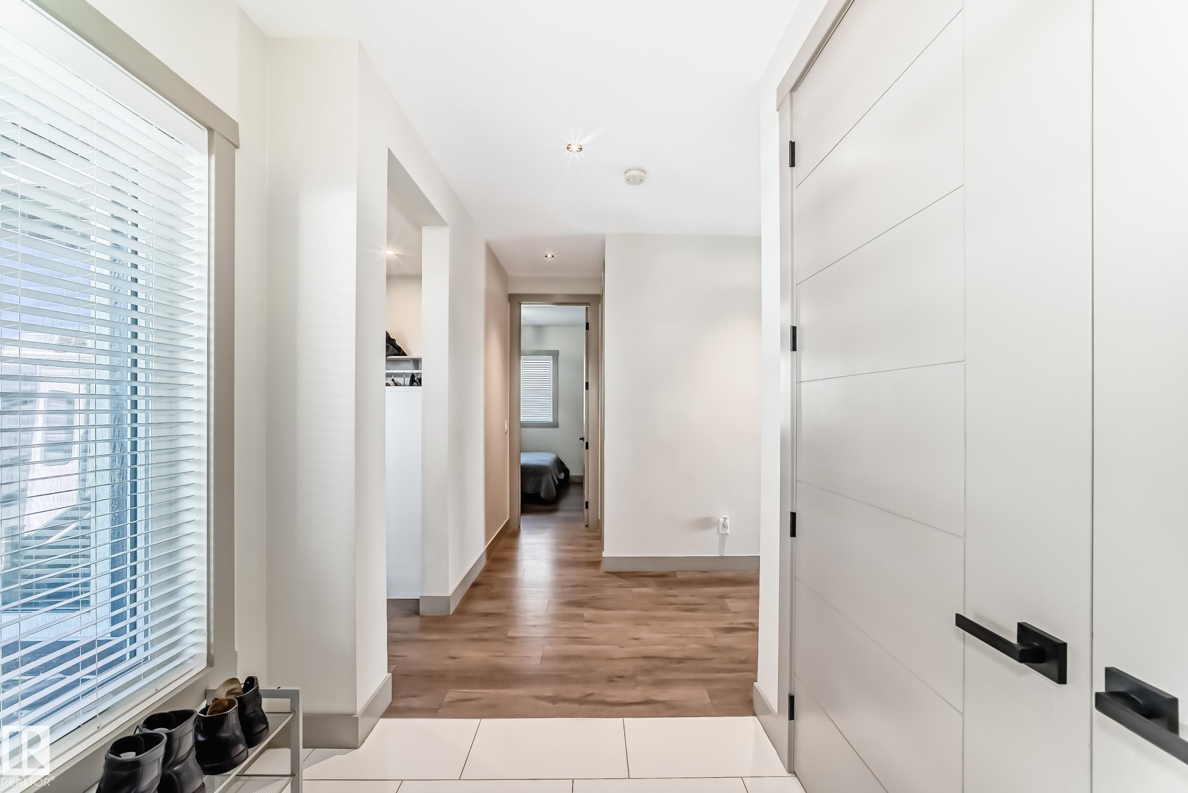 Bright entry area featuring a large window with white blinds, contemporary white doors with black hardware, recessed lighting, and wood-finish flooring transitioning to light-toned tile - 5263 47 Ave, Calmar, AB - Indoor Photo Showing Other Room