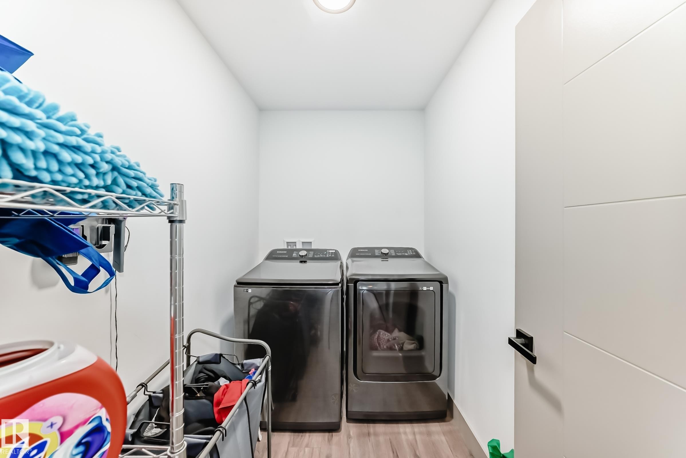 Dedicated laundry area featuring a washer and dryer set, wood-finish flooring, and a modern interior door with a black handle - 5263 47 Ave, Calmar, AB - Indoor Photo Showing Laundry Room