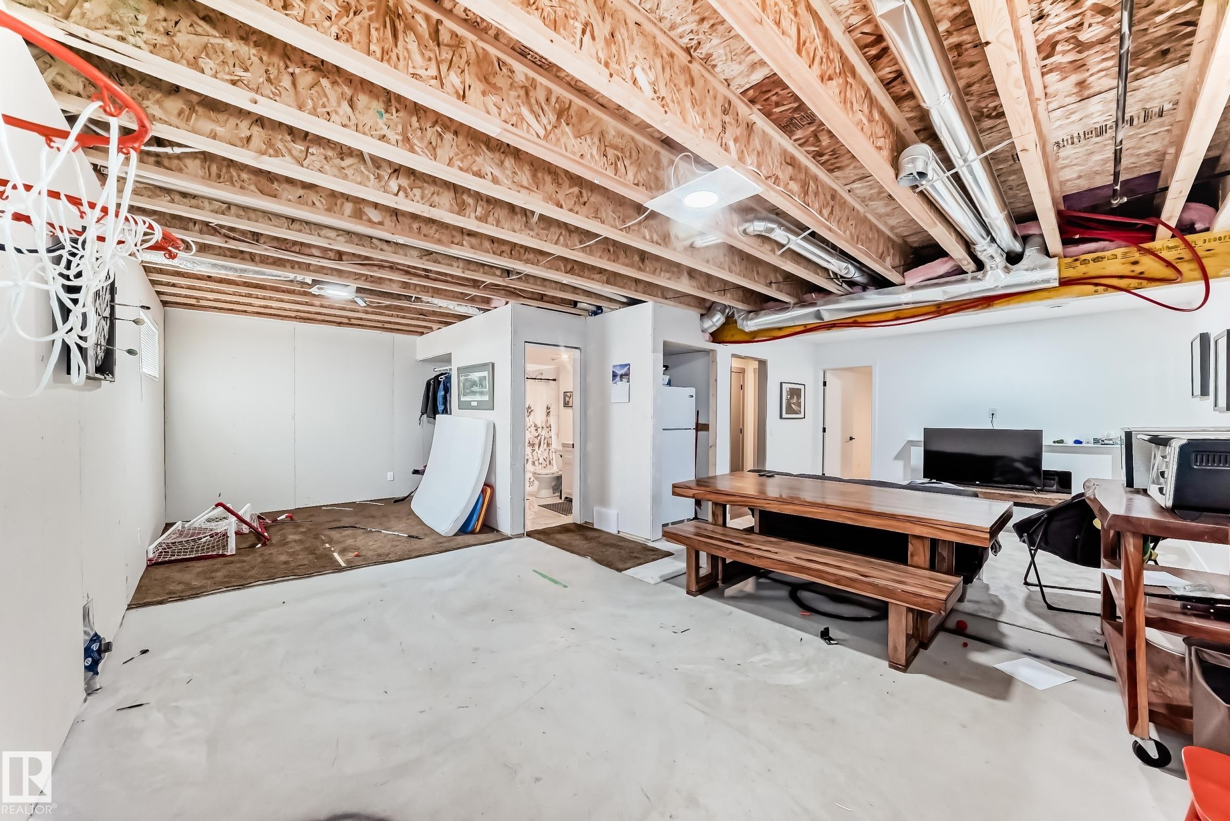 Unfinished basement with exposed wood joists and ductwork, featuring a partial wall enclosure housing a bathroom and a separate door leading to an additional space - 5263 47 Ave, Calmar, AB - Indoor Photo Showing Basement