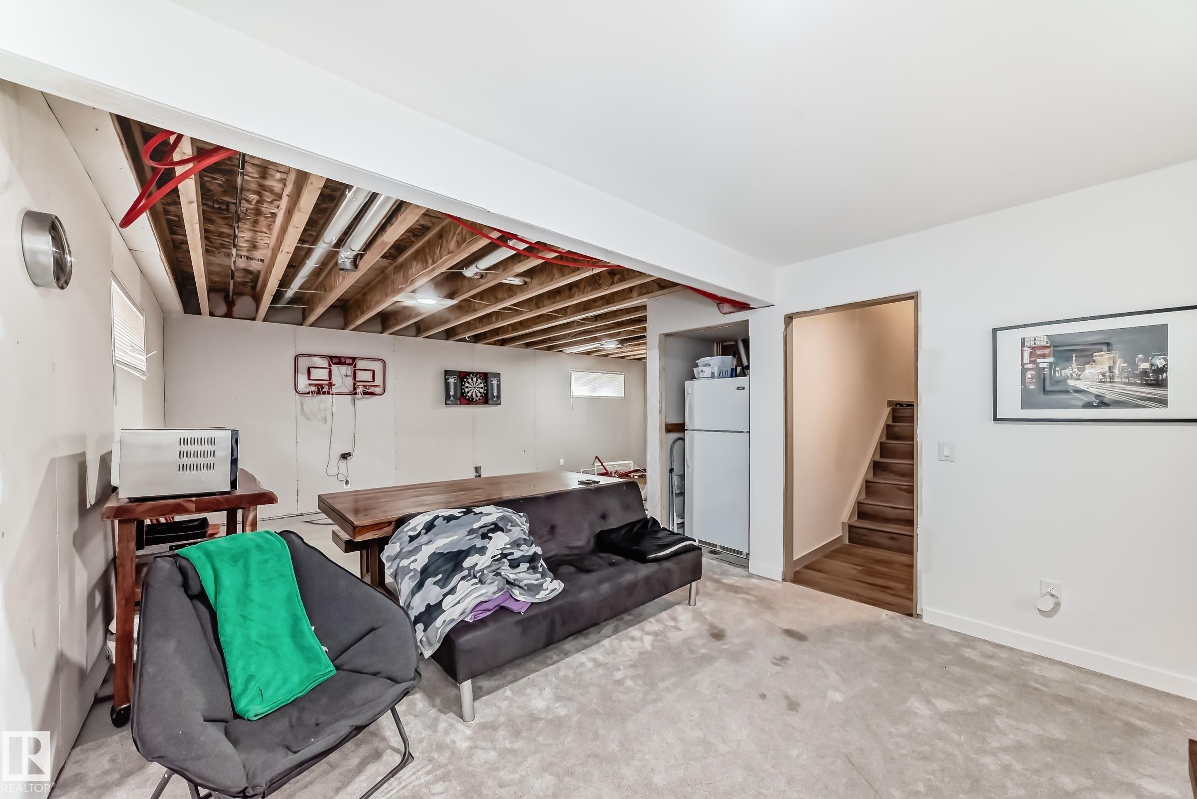 Unfinished basement space featuring exposed ceiling joists and utilities, painted white walls, and a light-colored carpeted floor - 5263 47 Ave, Calmar, AB - Indoor Photo Showing Other Room