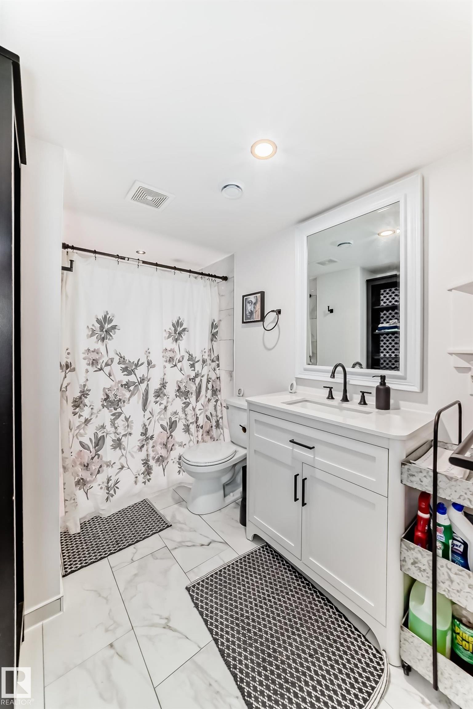 Contemporary bathroom featuring large format tile flooring, a white vanity with shaker-style cabinetry, and a rectangular mirror with a white frame - 5263 47 Ave, Calmar, AB - Indoor Photo Showing Bathroom