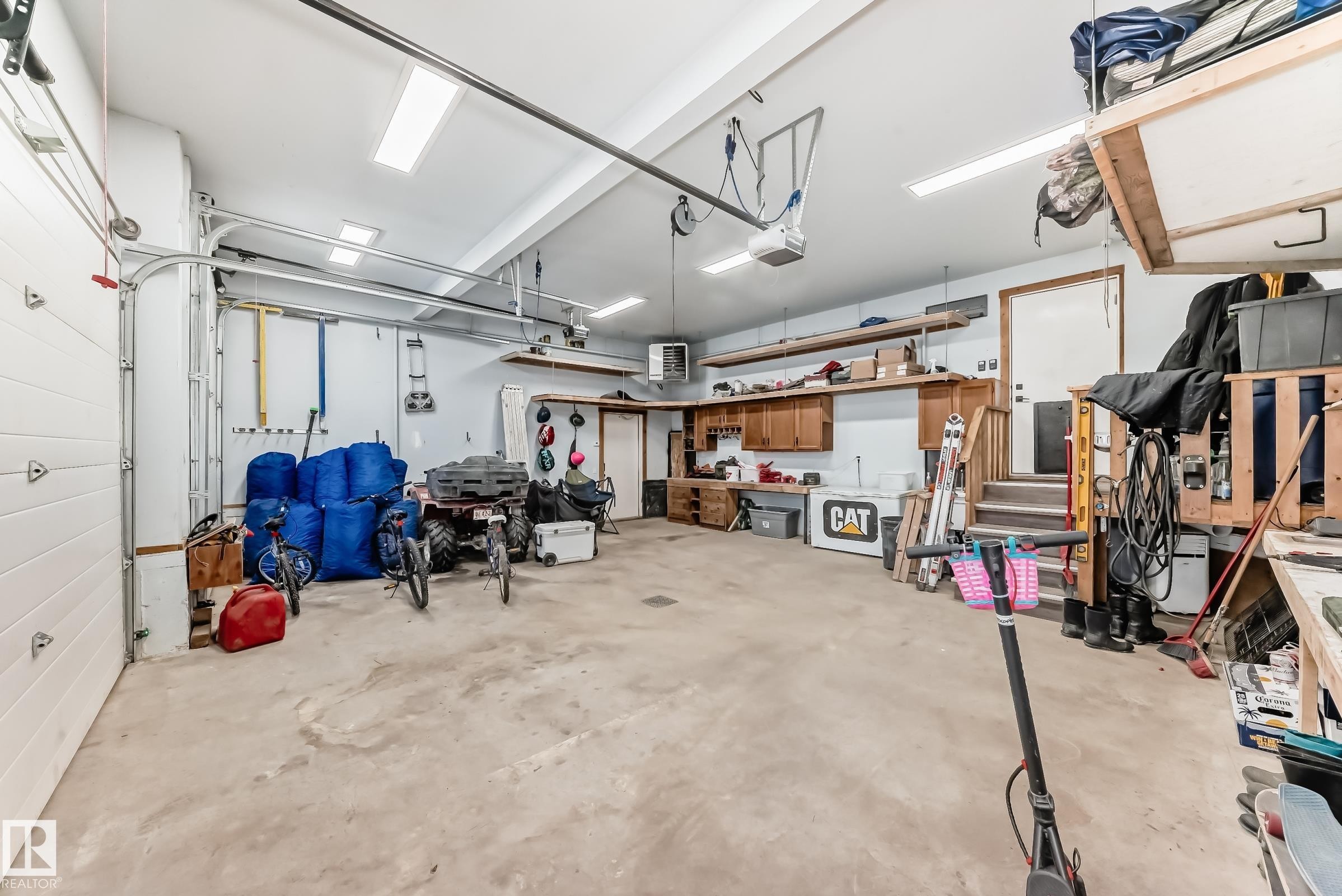 Spacious garage featuring concrete flooring, overhead fluorescent lighting, built-in wooden shelving, and an integrated workbench with cabinetry - 5263 47 Ave, Calmar, AB - Indoor Photo Showing Garage