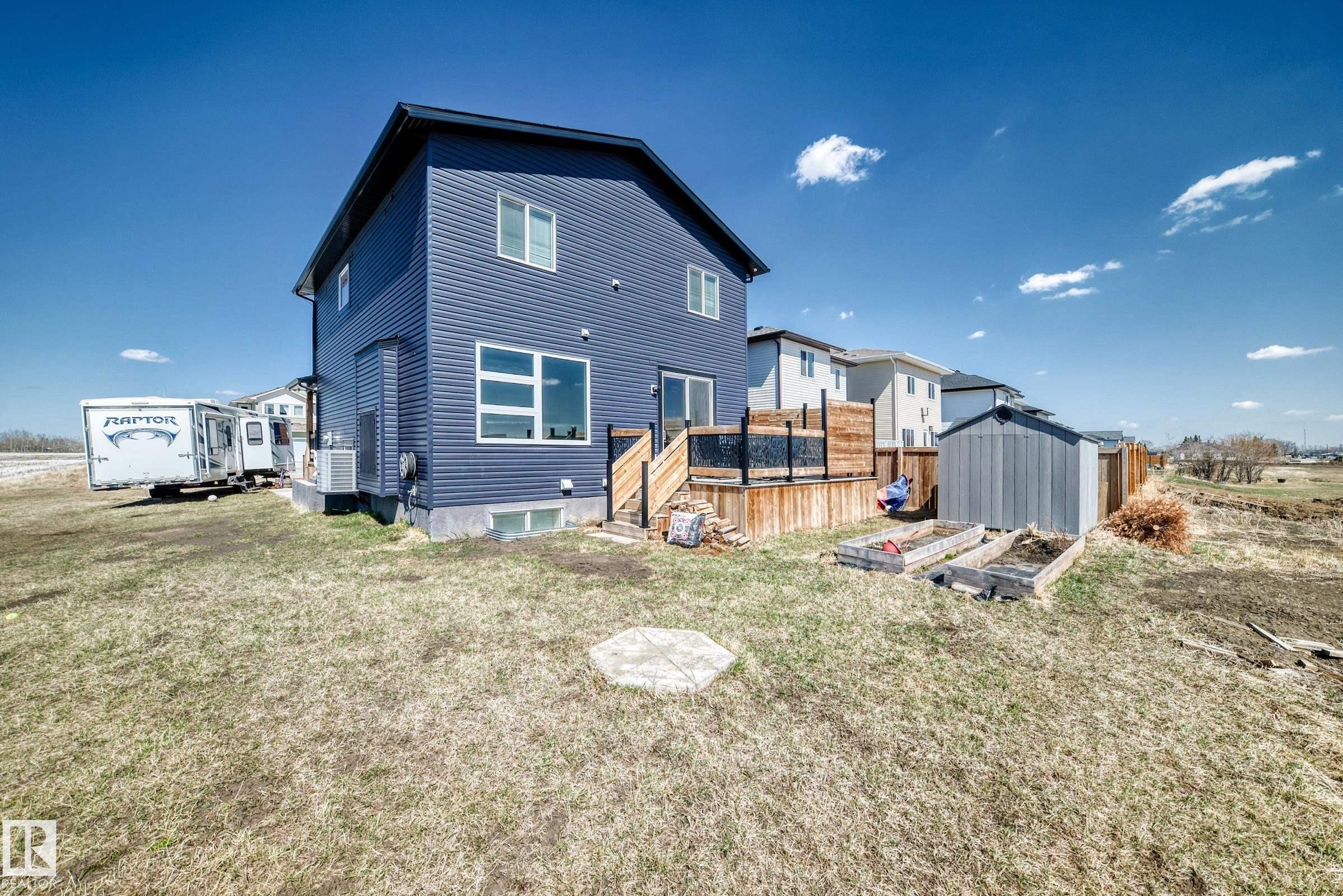 Modern two-story residence featuring blue horizontal siding, a rear wood deck with dark railing, a shed, and raised garden beds - 5263 47 Ave, Calmar, AB - Outdoor