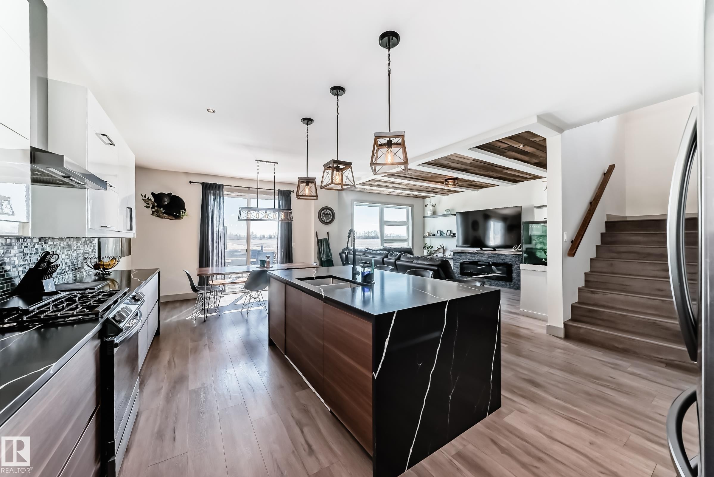 Spacious open-concept kitchen featuring a large waterfall island with a black and white veined countertop, stainless steel appliances, white gloss cabinetry, and wood-finish flooring throughout - 5263 47 Ave, Calmar, AB - Indoor Photo Showing Kitchen With Upgraded Kitchen