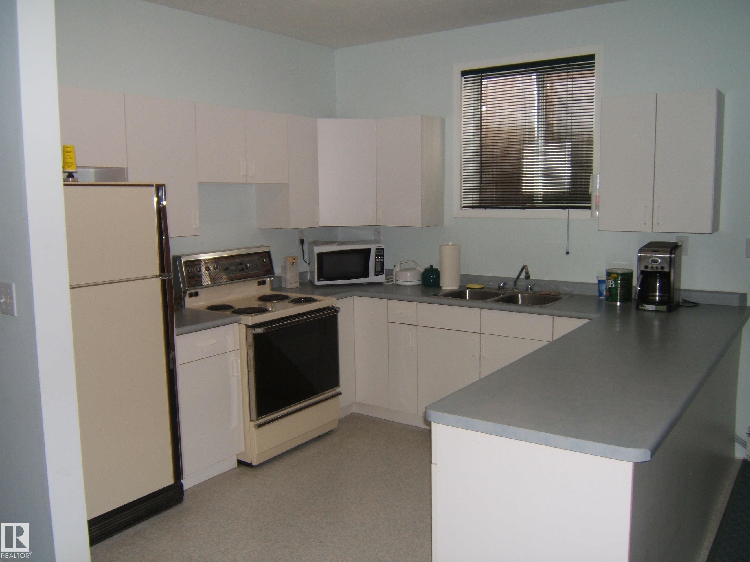 Kitchen featuring white cabinetry, a double basin sink, a window with horizontal blinds, a built-in oven with a stovetop, and a refrigerator - 4707 50 Street, Two Hills, AB - Indoor Photo Showing Kitchen With Double Sink