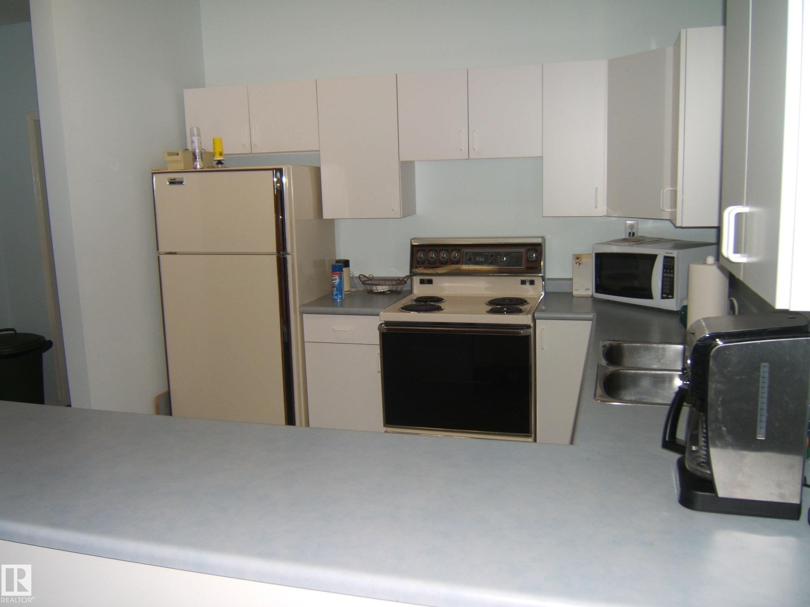 Kitchen featuring light cabinetry, a double basin stainless steel sink, and a light-colored countertop - 4707 50 Street, Two Hills, AB - Indoor Photo Showing Kitchen
