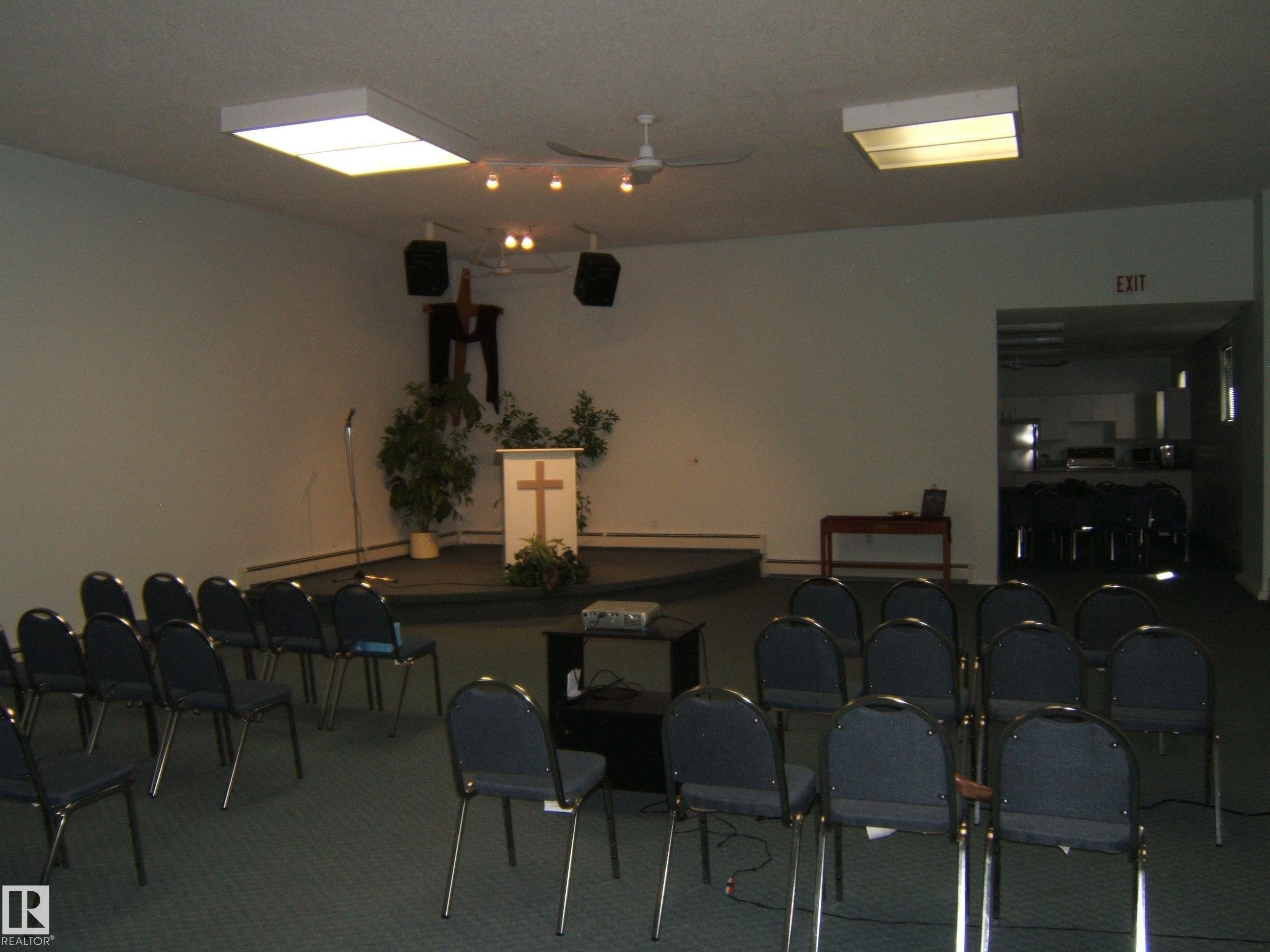 Carpeted room featuring a raised platform, recessed fluorescent lighting, and a ceiling fan - 4707 50 Street, Two Hills, AB - Indoor Photo Showing Other Room