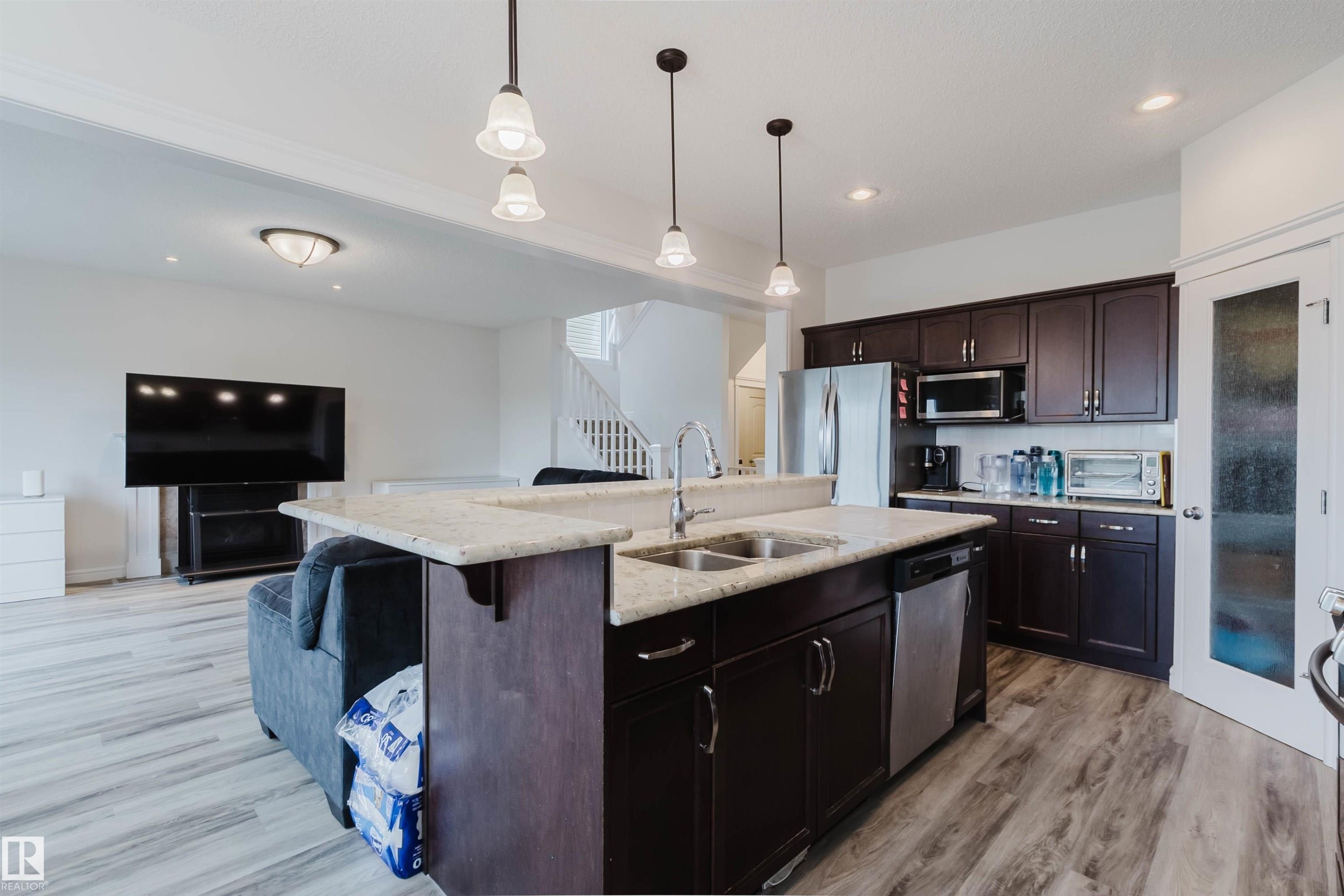 Open-concept kitchen featuring dark wood-finish cabinetry, a light-toned countertop, and stainless steel appliances - 17718 5A Avenue, Edmonton, AB - Indoor Photo Showing Kitchen With Double Sink