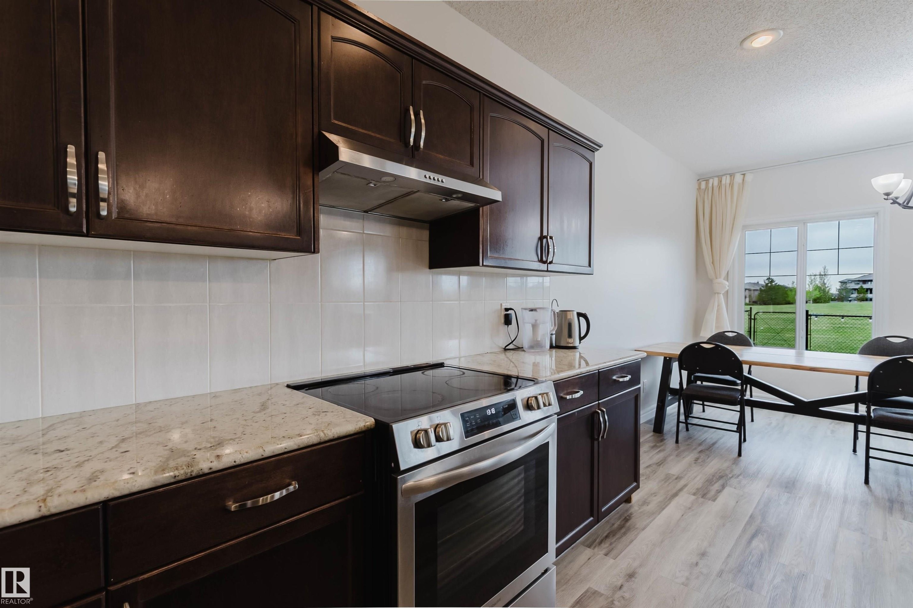 Kitchen featuring dark wood cabinetry, light-toned countertops, a stainless steel range with overhead ventilation, and white tile backsplash - 17718 5A Avenue, Edmonton, AB - Indoor Photo Showing Kitchen With Upgraded Kitchen