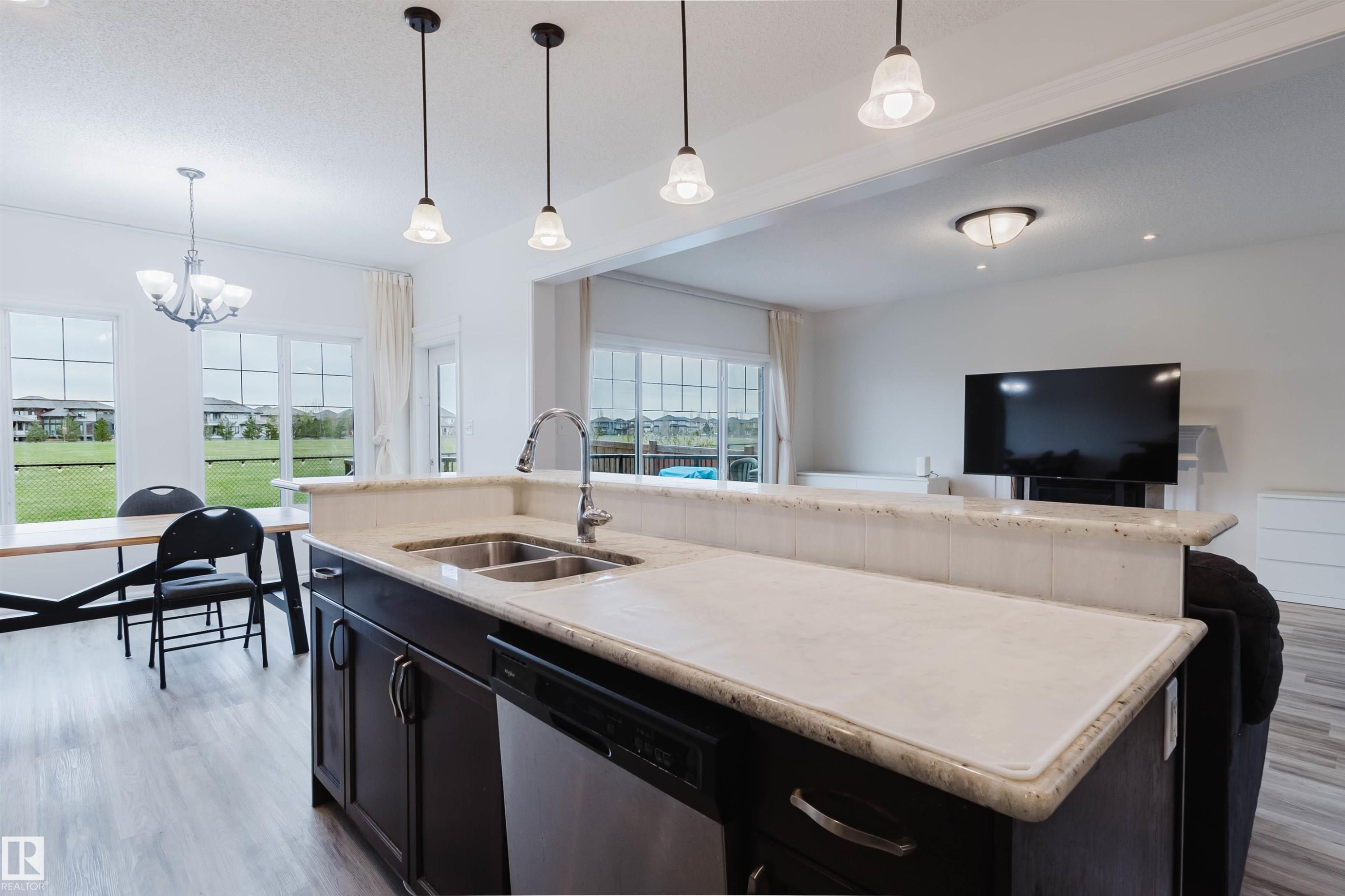 Kitchen island featuring a double basin stainless steel sink, a chrome gooseneck faucet, and light-toned stone countertops - 17718 5A Avenue, Edmonton, AB - Indoor Photo Showing Kitchen With Double Sink