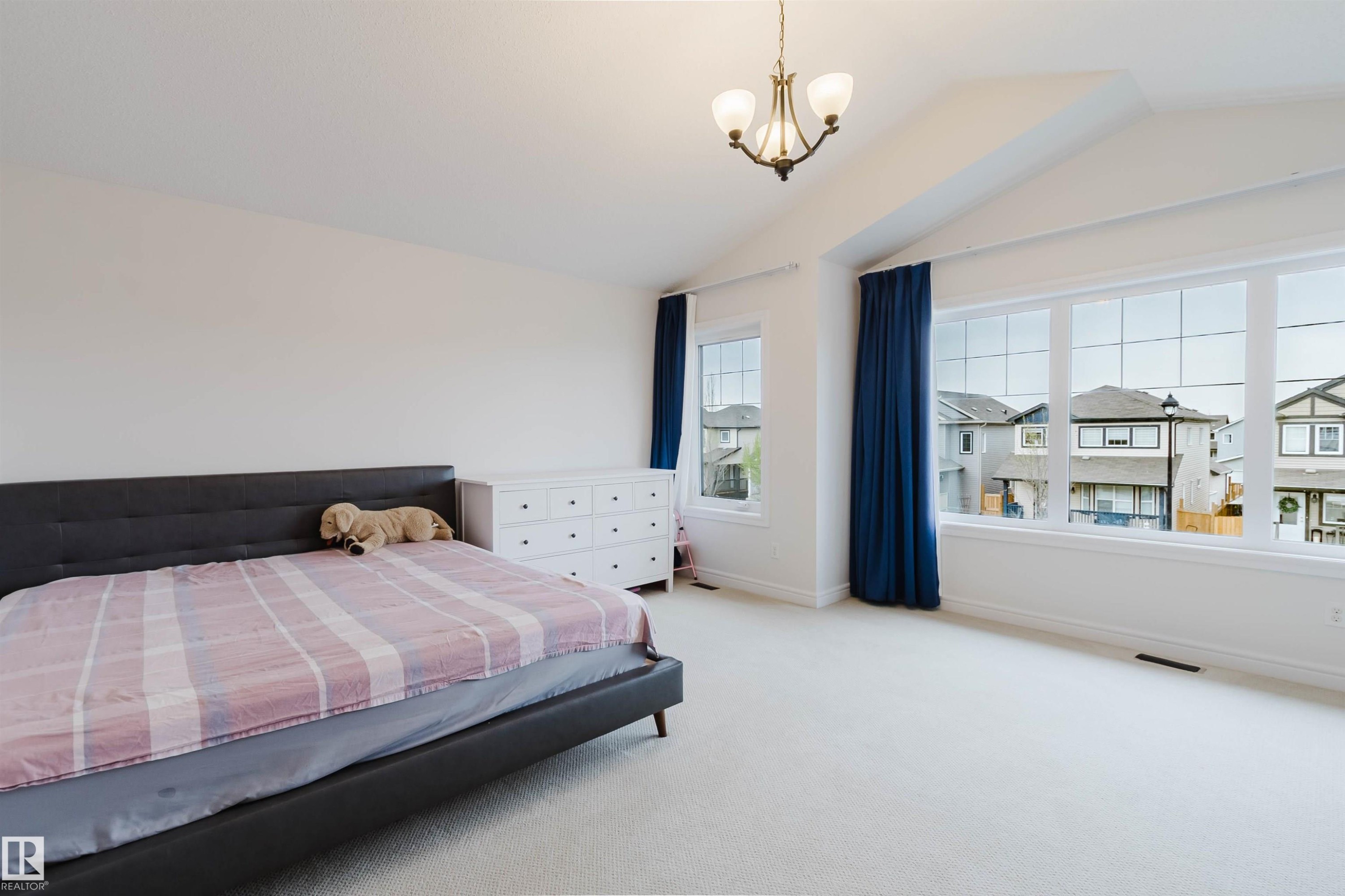 Spacious bedroom featuring vaulted ceilings, a central chandelier, multiple large windows, and light-toned wall-to-wall carpeting - 17718 5A Avenue, Edmonton, AB - Indoor Photo Showing Bedroom