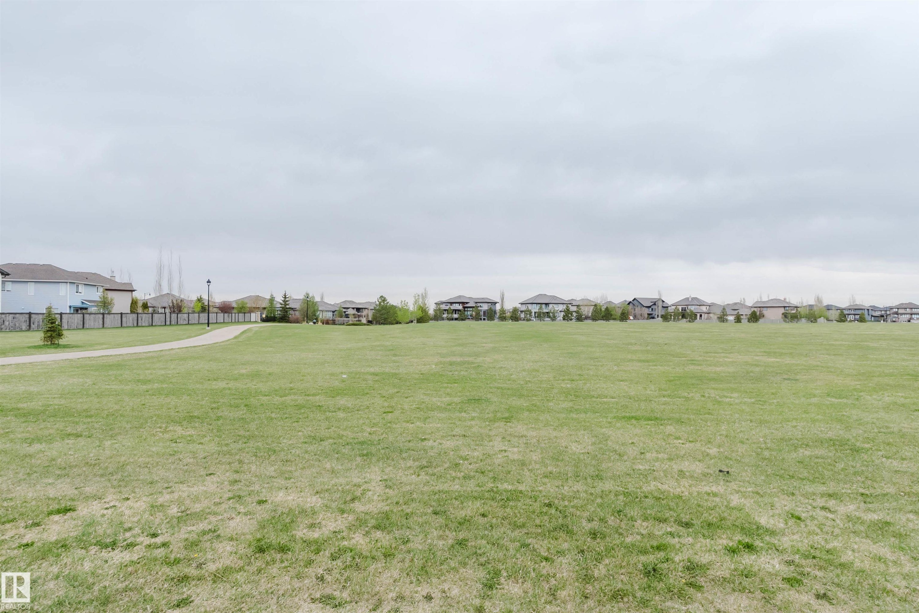Expansive green space featuring a paved walking path, surrounding residential properties, scattered trees, and a decorative fence line - 17718 5A Avenue, Edmonton, AB - Outdoor With View