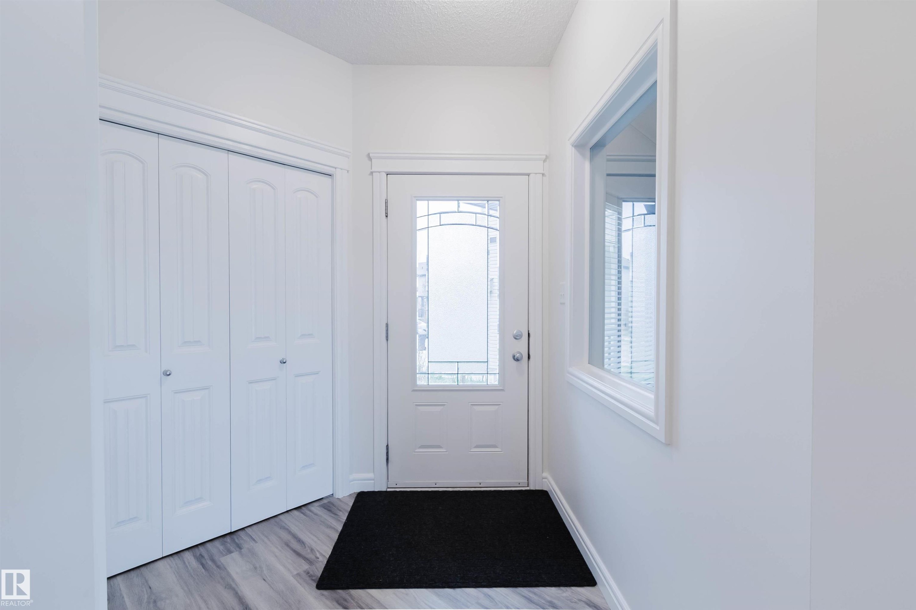 Entryway featuring a white door with decorative glass inserts, a single pane window, bi-fold closet doors, and wood-finish flooring - 17718 5A Avenue, Edmonton, AB - Indoor Photo Showing Other Room