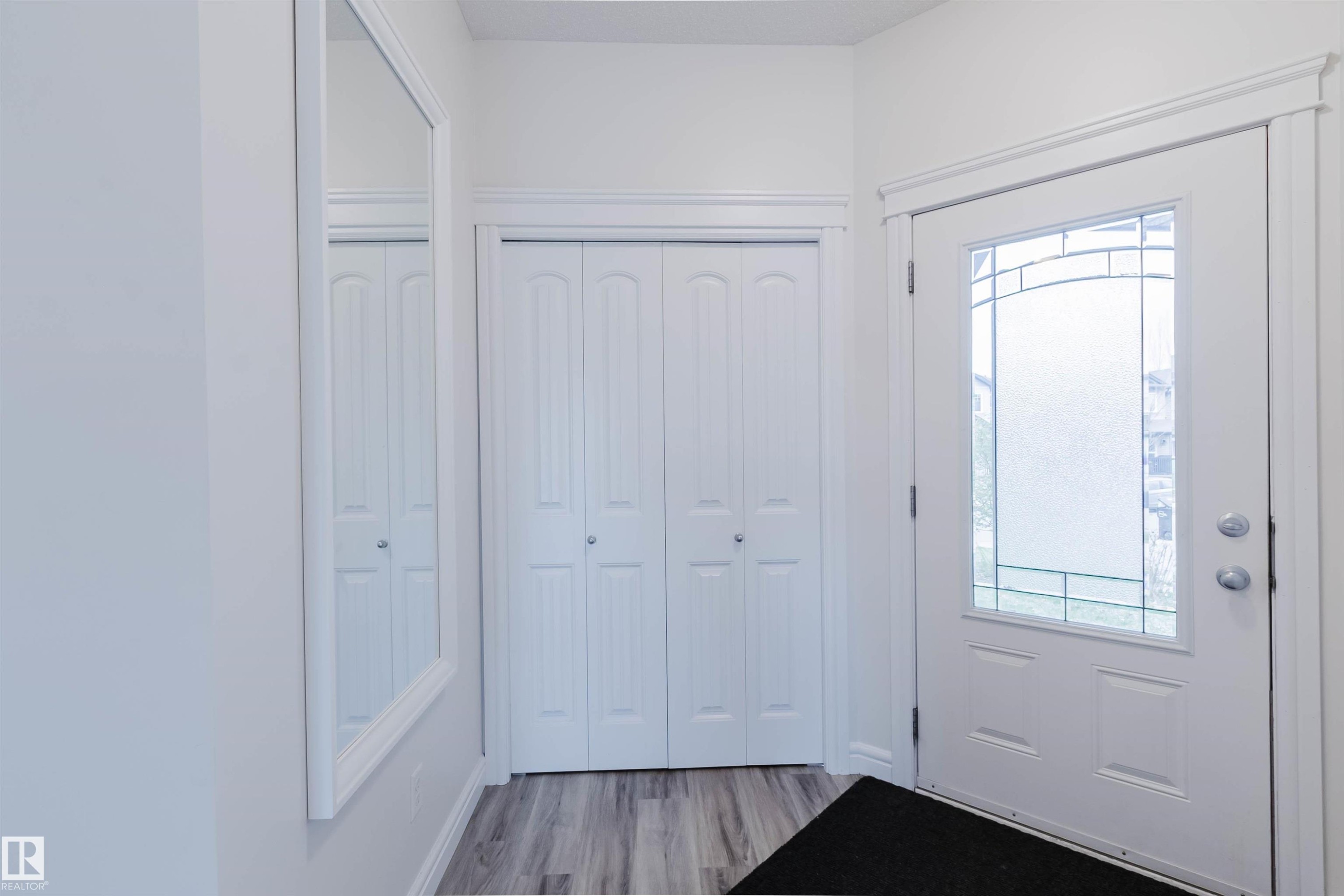 Entryway featuring a white front door with decorative glass inserts, bi-fold closet doors, a framed wall mirror, light wood-finish flooring, and white trim - 17718 5A Avenue, Edmonton, AB - Indoor Photo Showing Other Room