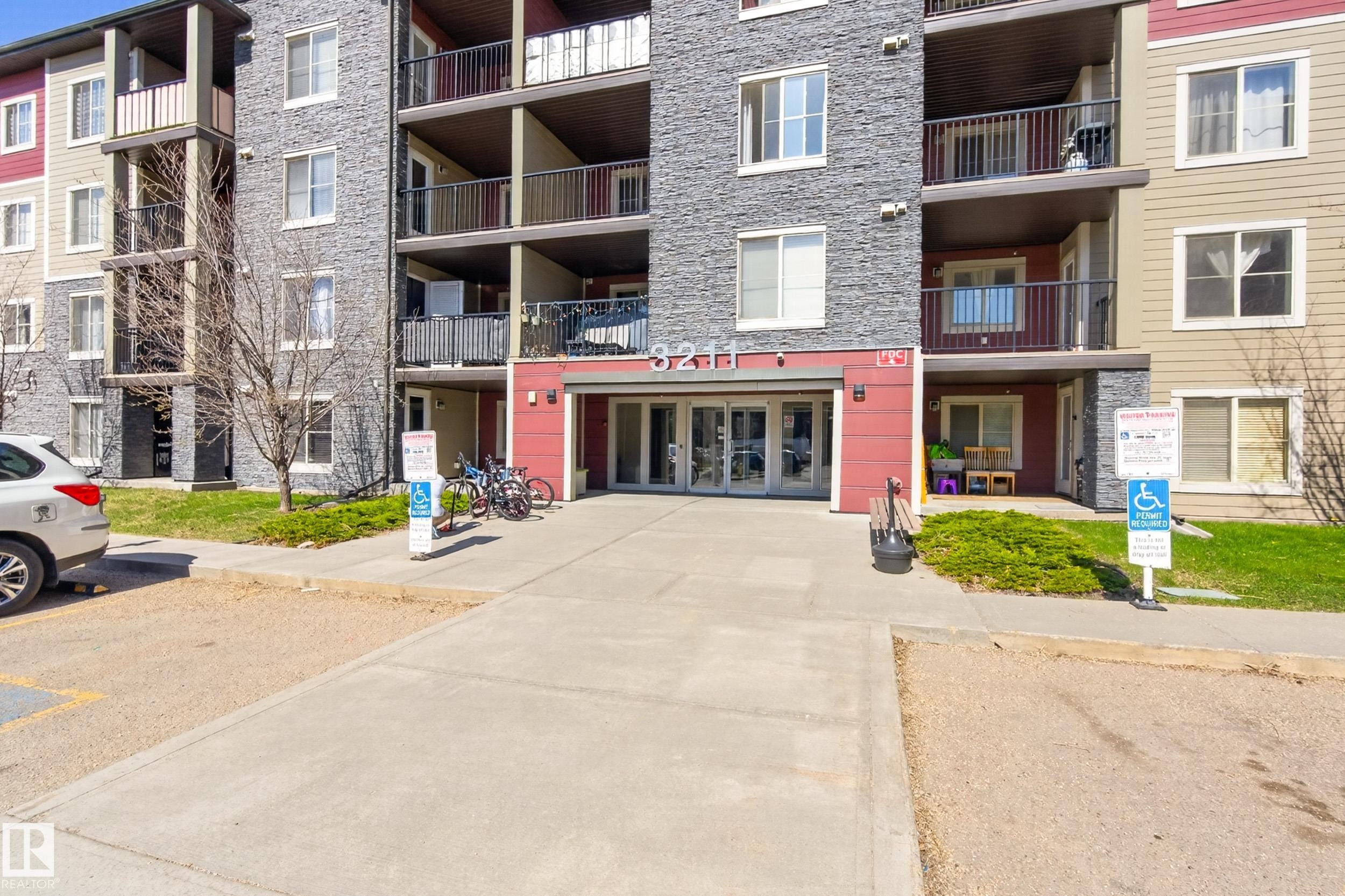 Multi-story building exterior featuring a stone facade and red accent panels, with individual balconies and ground-level patios - 314 3211 James Mowatt Trail Sw, Edmonton, AB - Outdoor With Facade