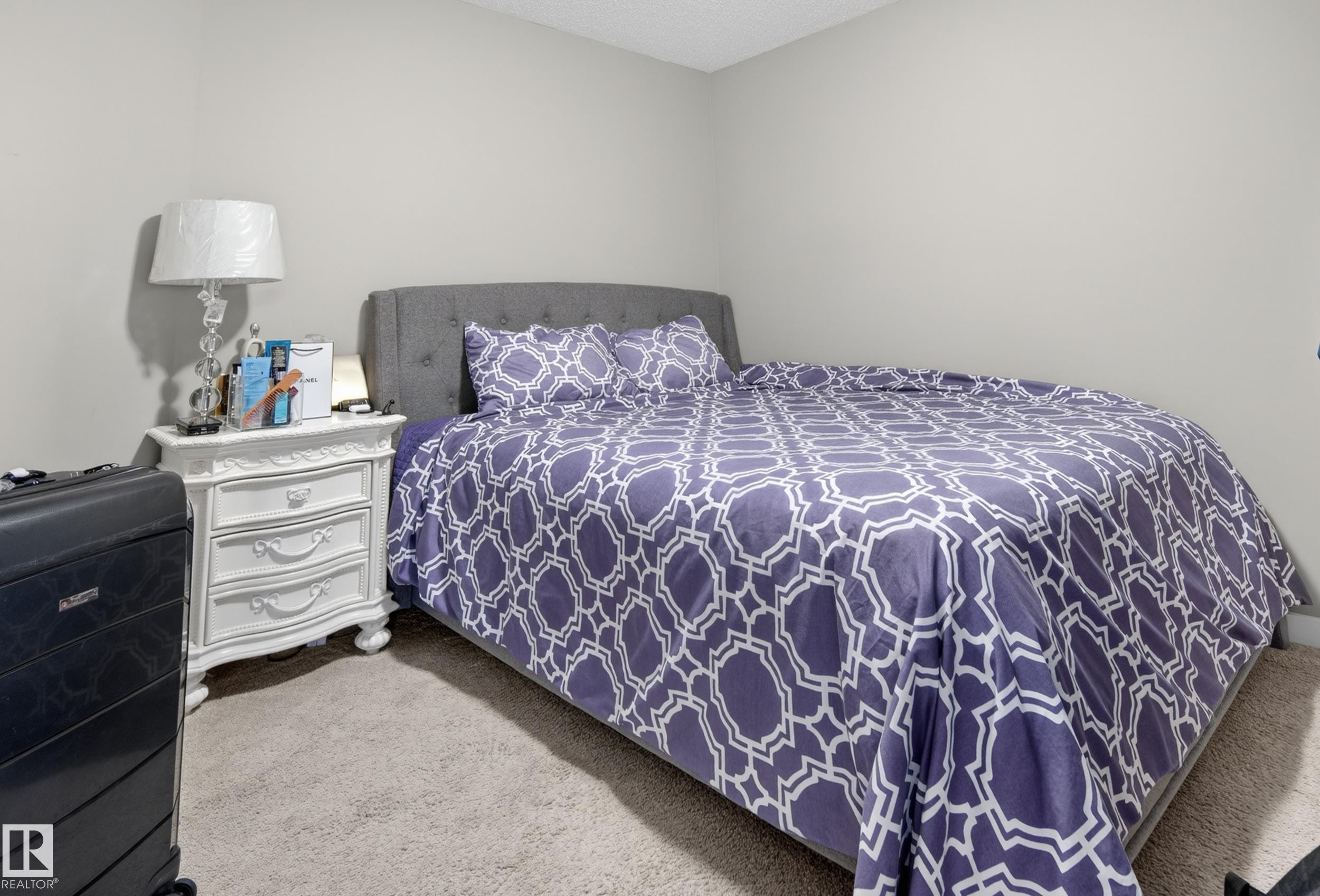 Carpeted room featuring light gray walls, a textured ceiling, and a built-in upholstered headboard - 314 3211 James Mowatt Trail Sw, Edmonton, AB - Indoor Photo Showing Bedroom