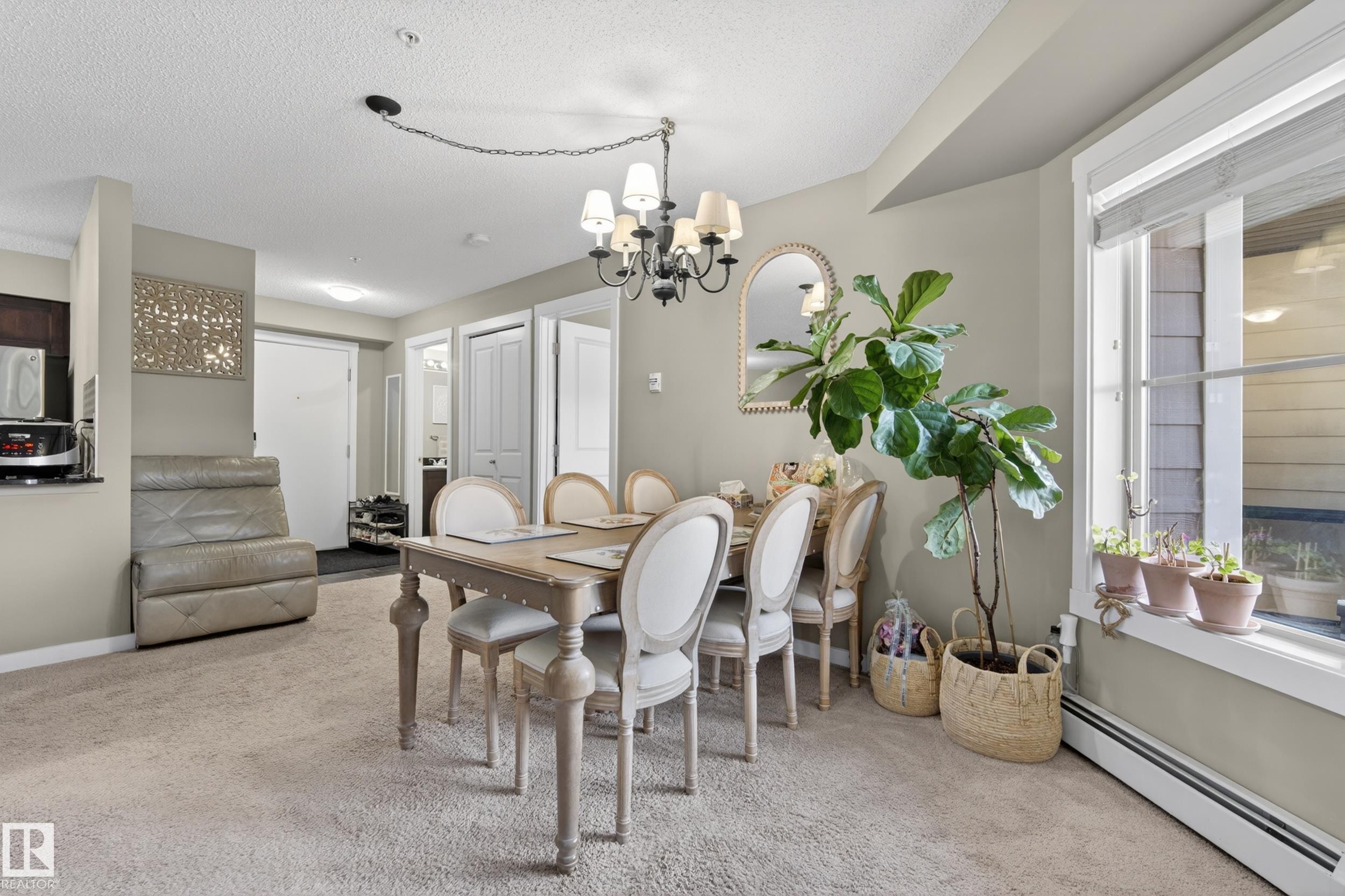 Open-concept dining area featuring a chandelier, a large window, and light-colored carpeting - 314 3211 James Mowatt Trail Sw, Edmonton, AB - Indoor Photo Showing Dining Room