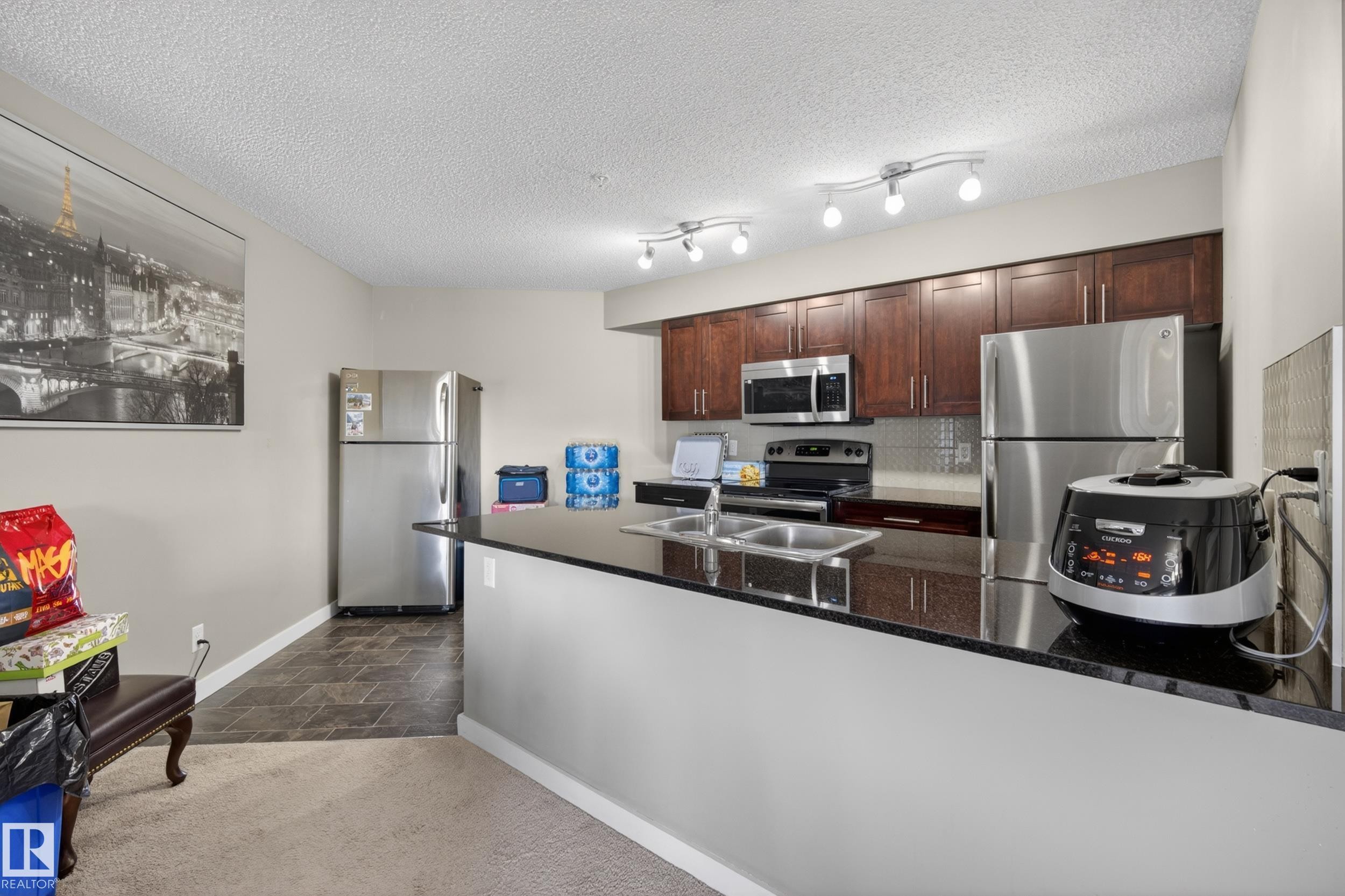 Kitchen featuring dark wood-finish cabinetry, black countertops, and stainless steel appliances - 314 3211 James Mowatt Trail Sw, Edmonton, AB - Indoor Photo Showing Kitchen With Stainless Steel Kitchen With Double Sink