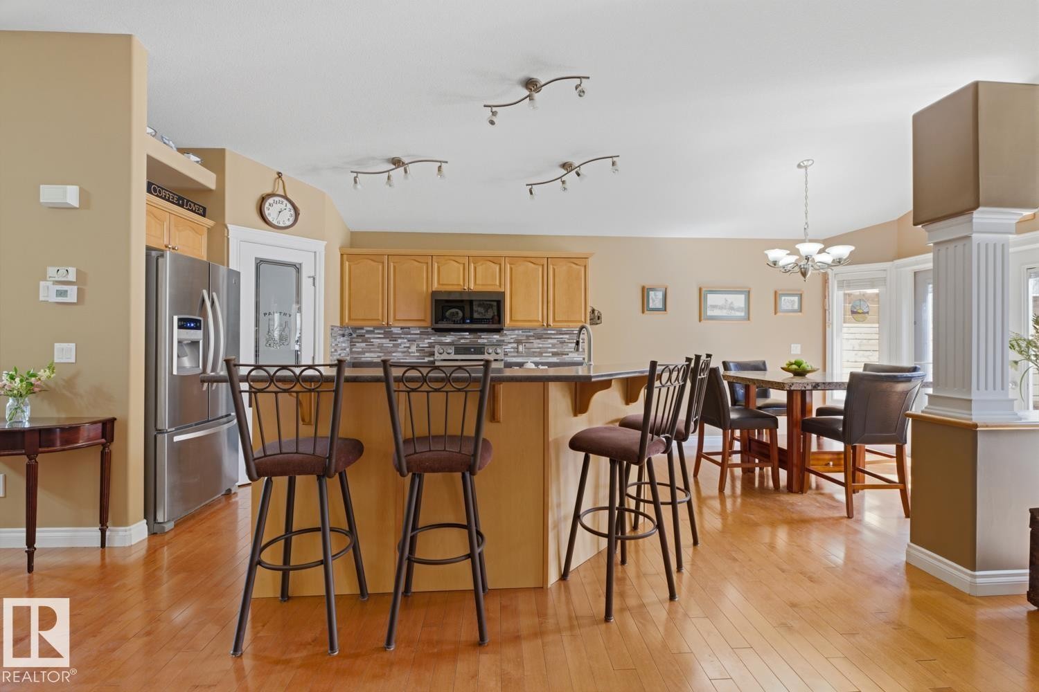 Open-concept kitchen and dining area featuring warm wood-finish flooring, light wood cabinetry, a stainless steel refrigerator, and a tiled kitchen backsplash - 9 Danfield Place, Spruce Grove, AB - Indoor Photo Showing Kitchen