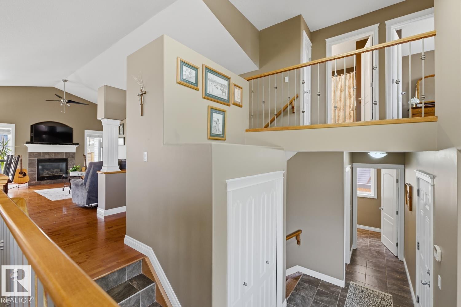 Multi-level interior featuring wood-finish flooring, a tiled fireplace with a mantel, vaulted ceilings, a ceiling fan, and a wood railing with metal spindles - 9 Danfield Place, Spruce Grove, AB - Indoor Photo Showing Other Room With Fireplace