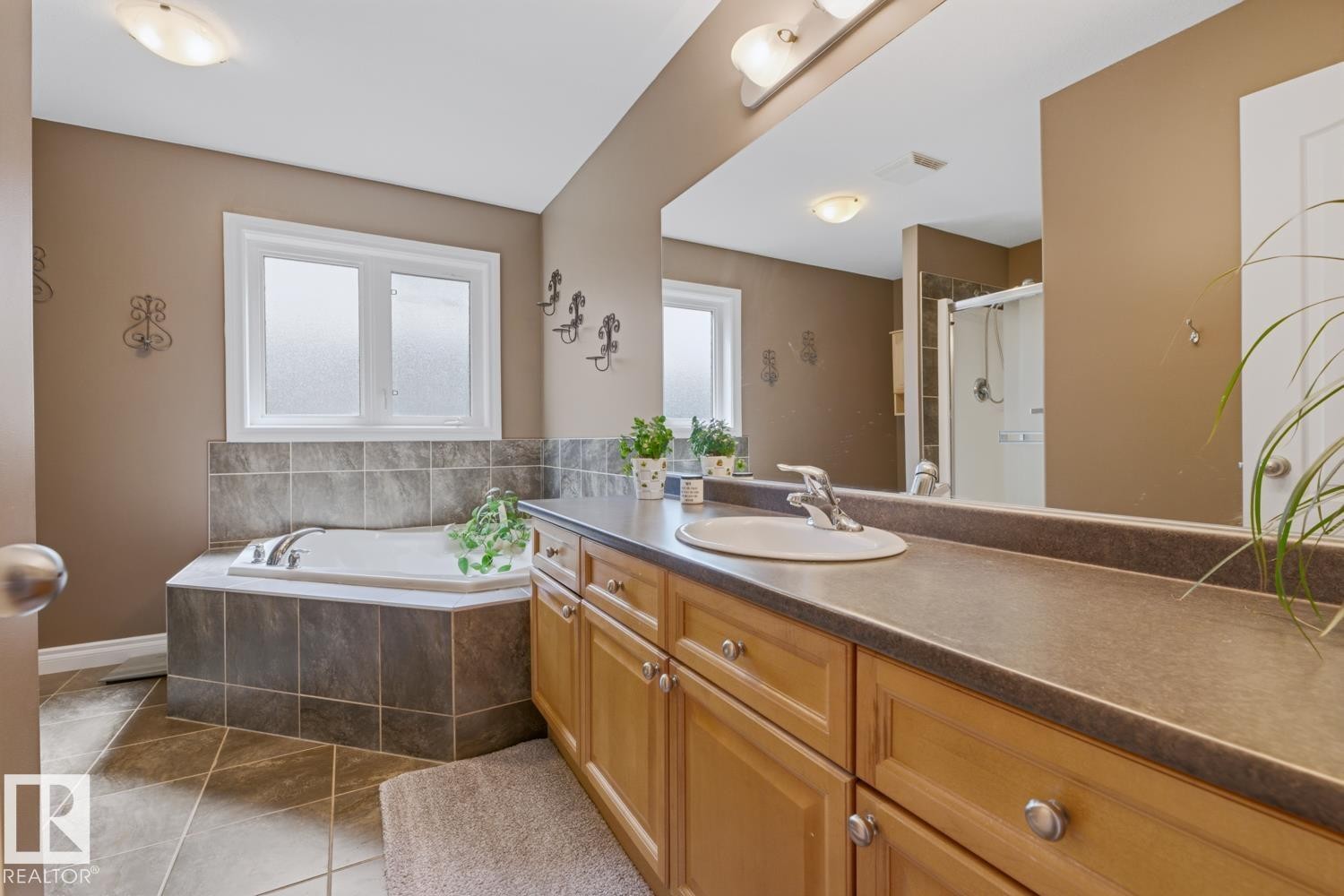 Bathroom featuring a corner soaking tub with tile surround, a double-door wood-finish vanity with a single basin, a large wall-mounted mirror, and tile flooring - 9 Danfield Place, Spruce Grove, AB - Indoor Photo Showing Bathroom
