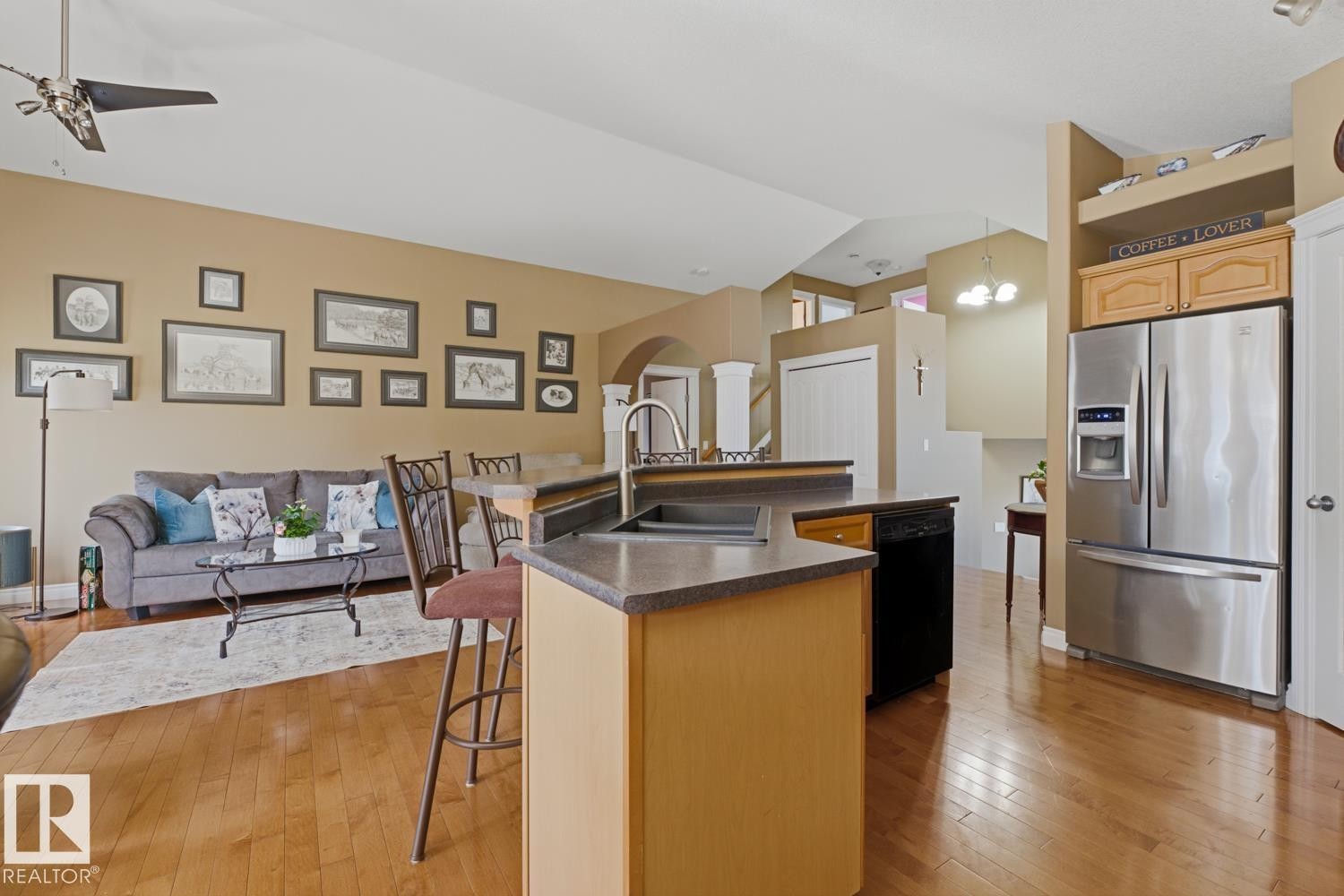 Open-concept living space featuring wood-finish flooring, a kitchen island with integrated sink, stainless steel French door refrigerator, and recessed lighting - 9 Danfield Place, Spruce Grove, AB - Indoor Photo Showing Kitchen With Double Sink