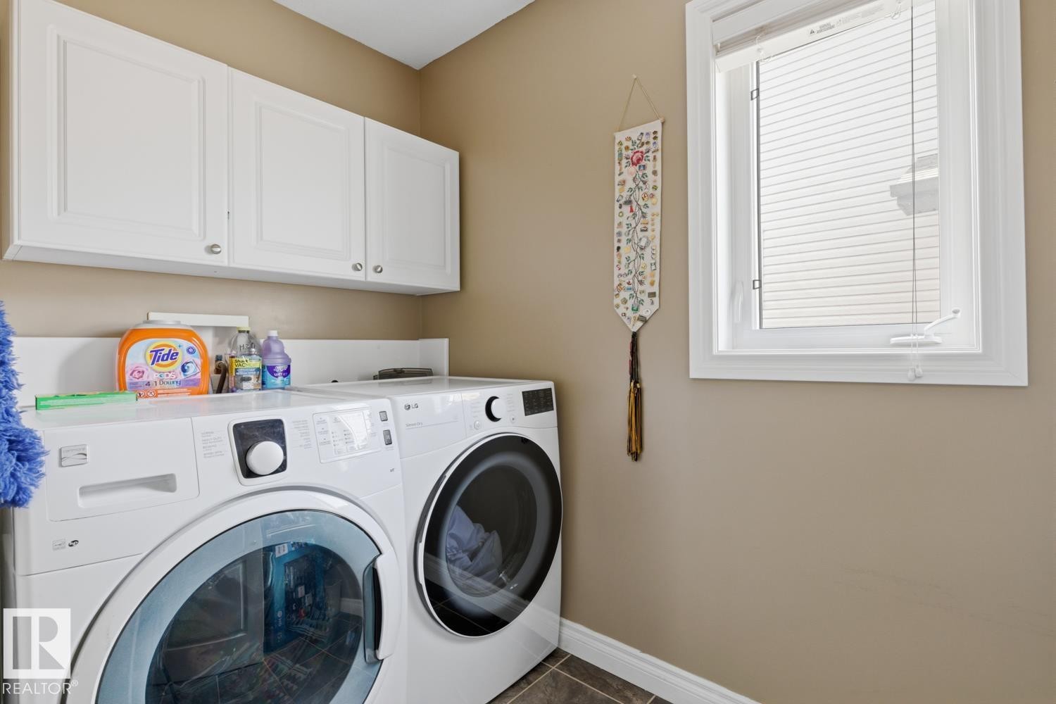 Dedicated laundry area featuring a front-loading washer and dryer, upper cabinetry with white shaker-style doors, a functional window, and neutral wall paint - 9 Danfield Place, Spruce Grove, AB - Indoor Photo Showing Laundry Room