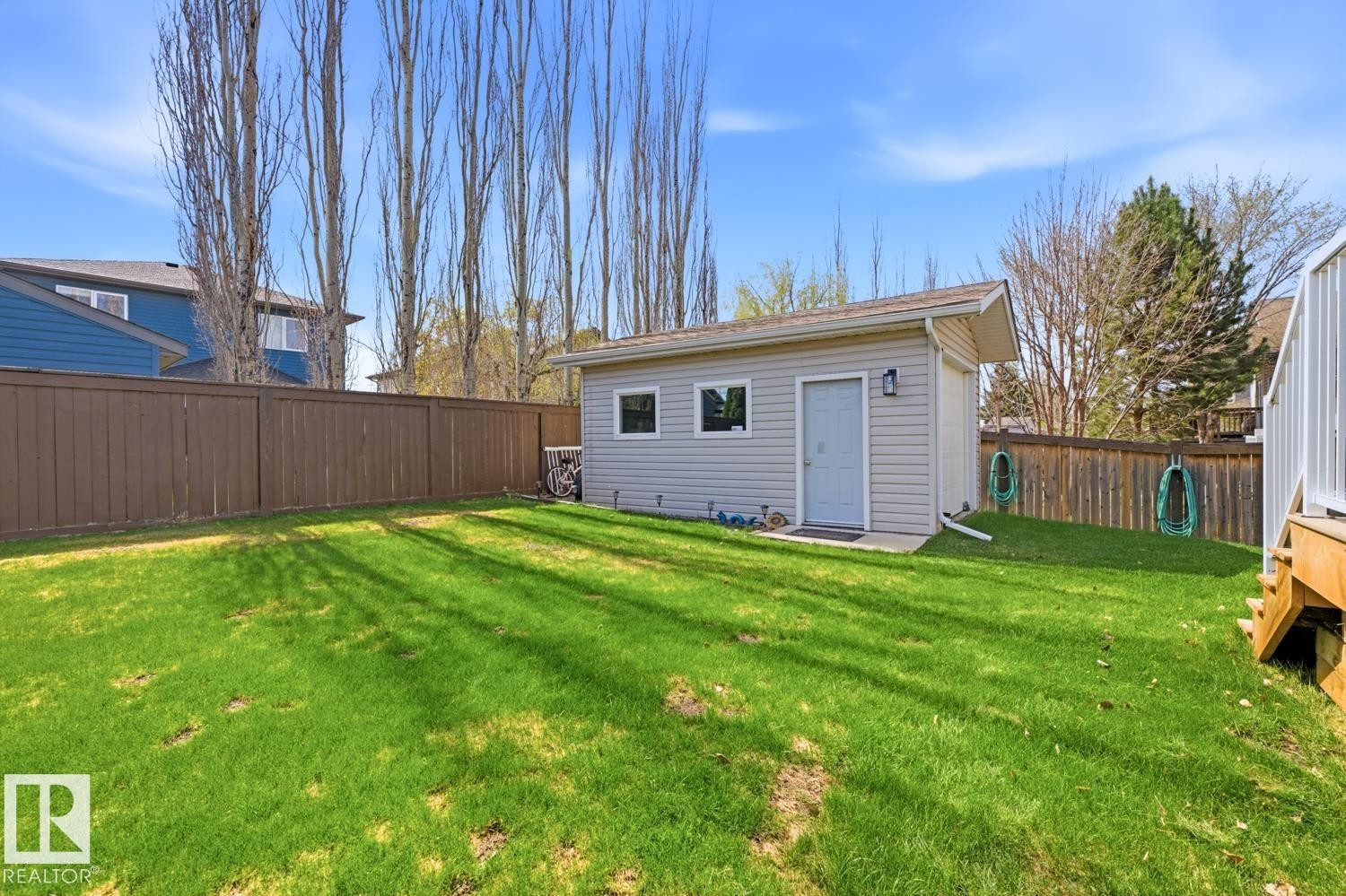 Expansive green lawn with a detached auxiliary building featuring light-colored siding, multiple windows, and a side entry door - 9 Danfield Place, Spruce Grove, AB - Outdoor