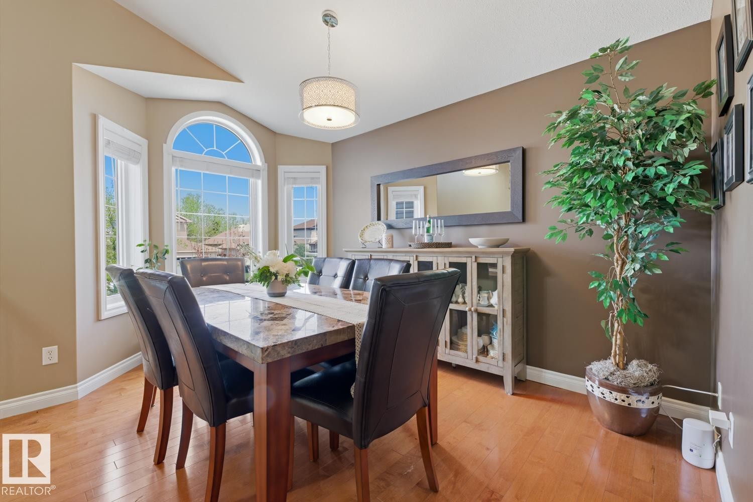 Dining area featuring a prominent arched window, wood-finish flooring, and a decorative drum pendant light fixture - 9 Danfield Place, Spruce Grove, AB - Indoor Photo Showing Dining Room