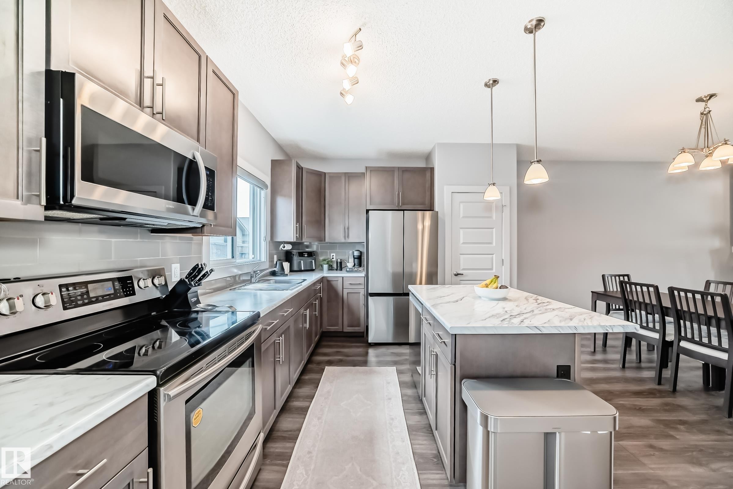 Gourmet kitchen featuring stainless steel appliances, wood-finish cabinetry, light-toned countertops, and a subway tile backsplash - 6919 Cardinal Wynd, Edmonton, AB - Indoor Photo Showing Kitchen With Stainless Steel Kitchen With Upgraded Kitchen