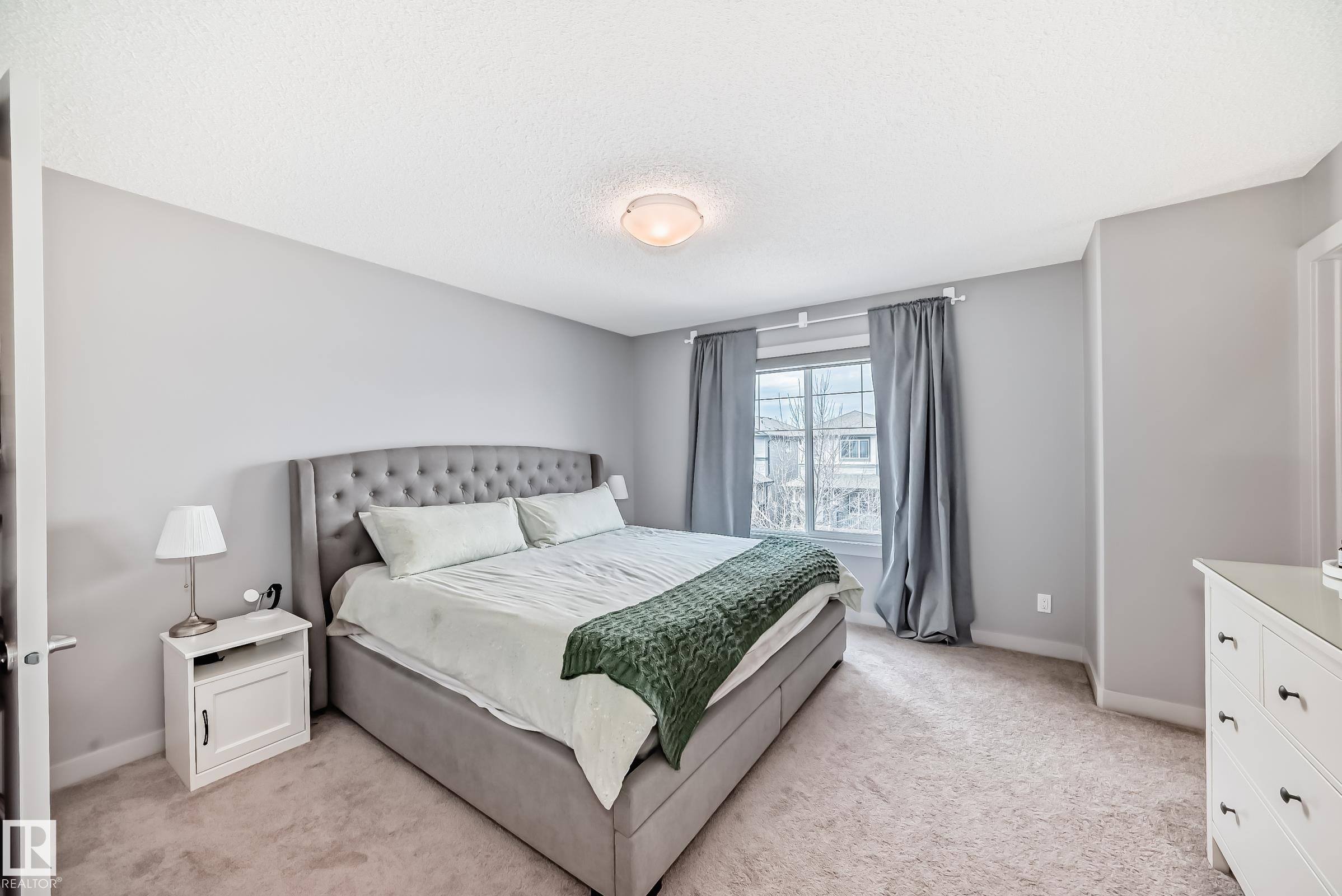 Carpeted bedroom featuring neutral grey wall paint, a double window with drapes, and a ceiling-mounted light fixture - 6919 Cardinal Wynd, Edmonton, AB - Indoor Photo Showing Bedroom