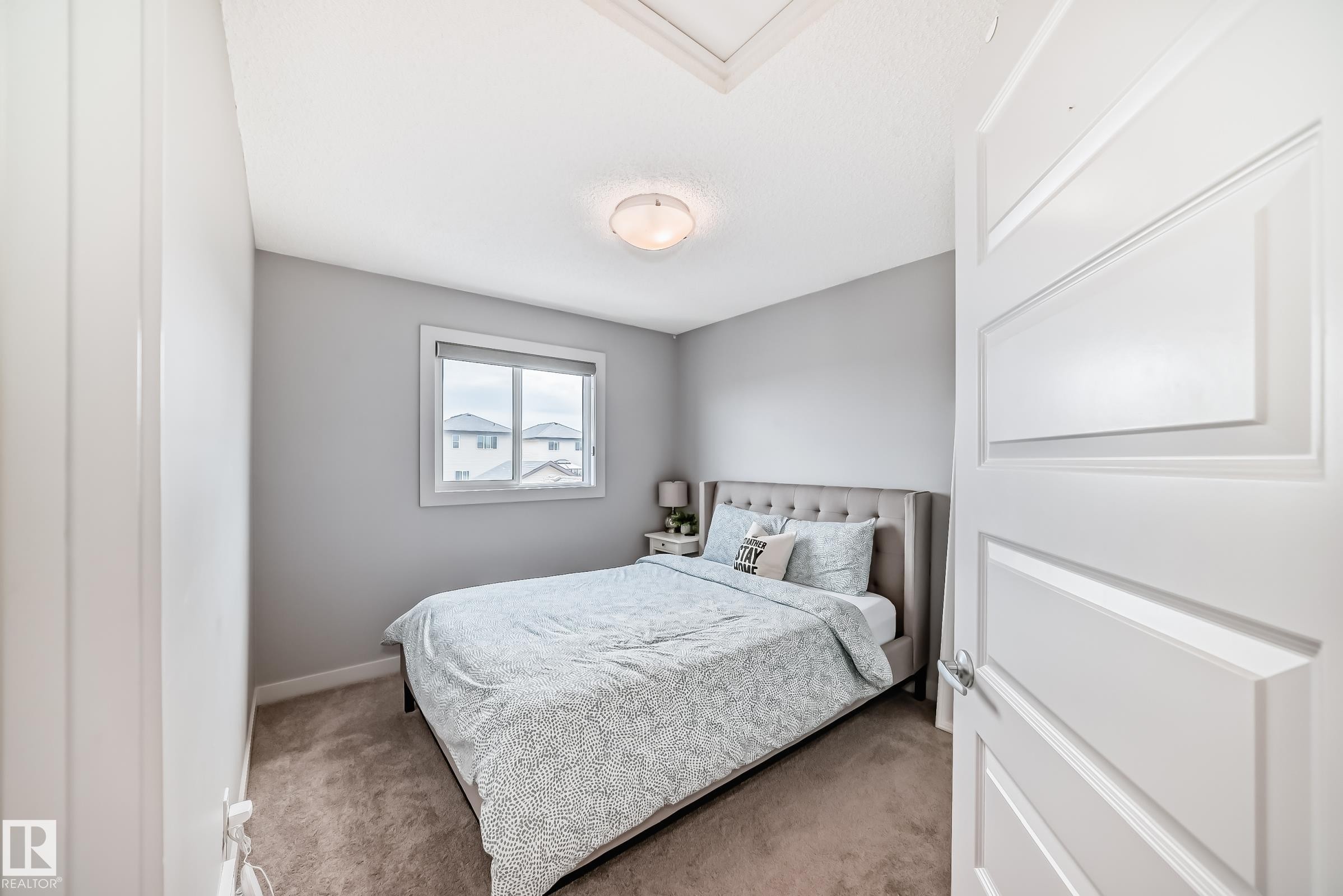 Carpeted interior room featuring a window, light gray walls, white trim, and a ceiling-mounted light fixture - 6919 Cardinal Wynd, Edmonton, AB - Indoor Photo Showing Bedroom