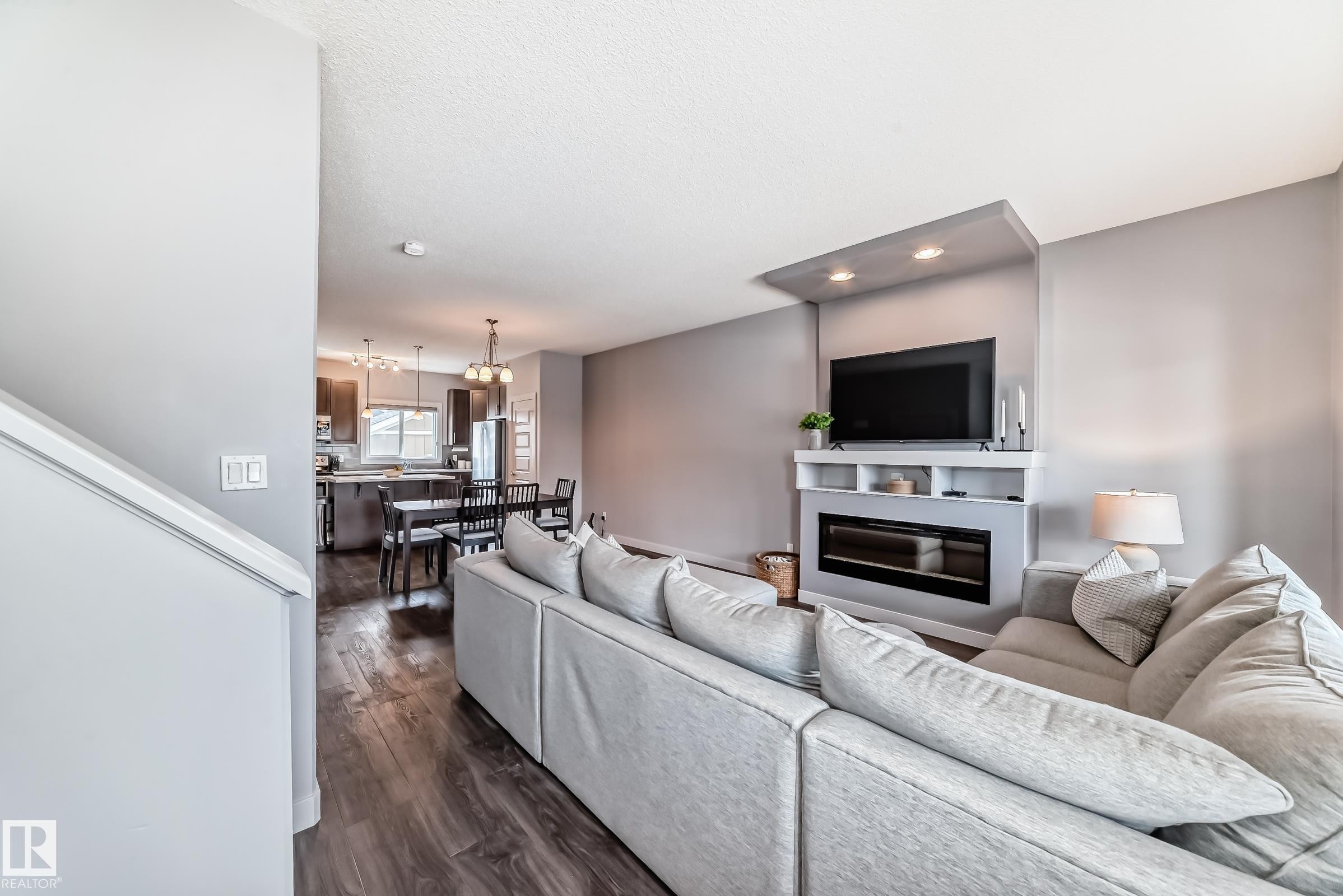 Open concept living space featuring wood-finish flooring, a built-in media console with an electric fireplace, recessed lighting, and a defined dining area with pendant lighting - 6919 Cardinal Wynd, Edmonton, AB - Indoor Photo Showing Living Room With Fireplace