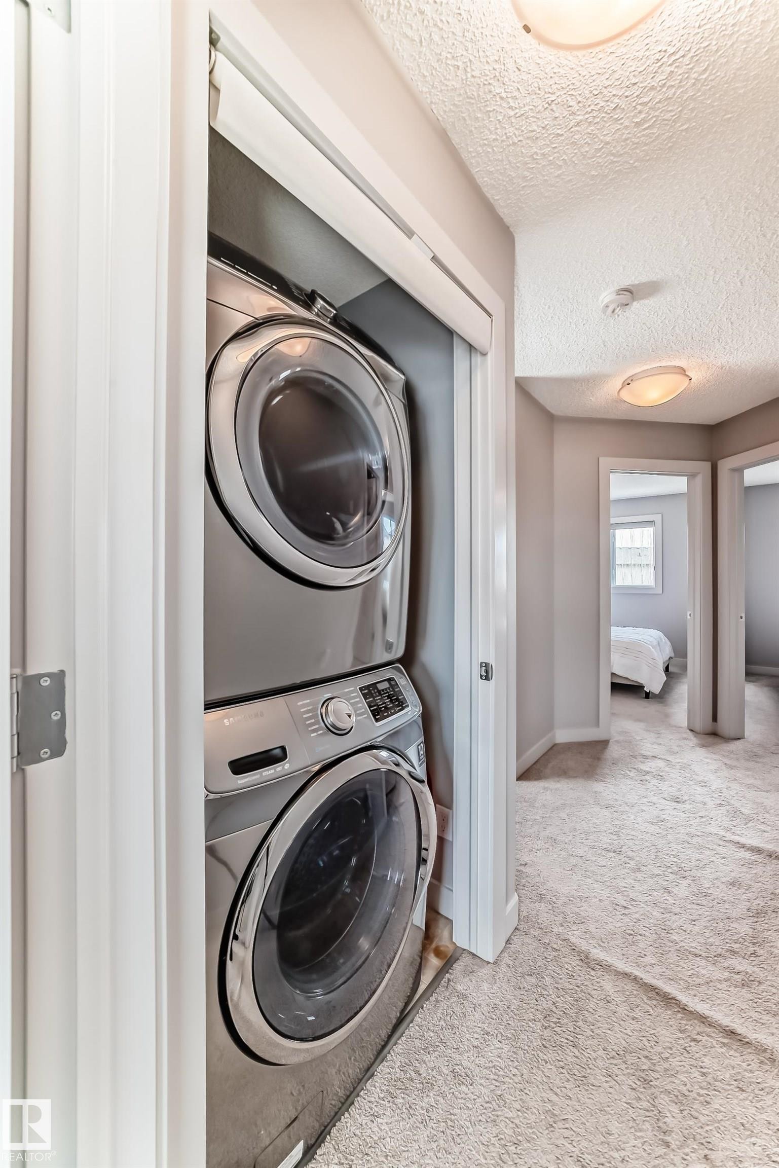 Stacked laundry appliances within a dedicated closet, featuring a front-loading washer and dryer - 6919 Cardinal Wynd, Edmonton, AB - Indoor Photo Showing Laundry Room