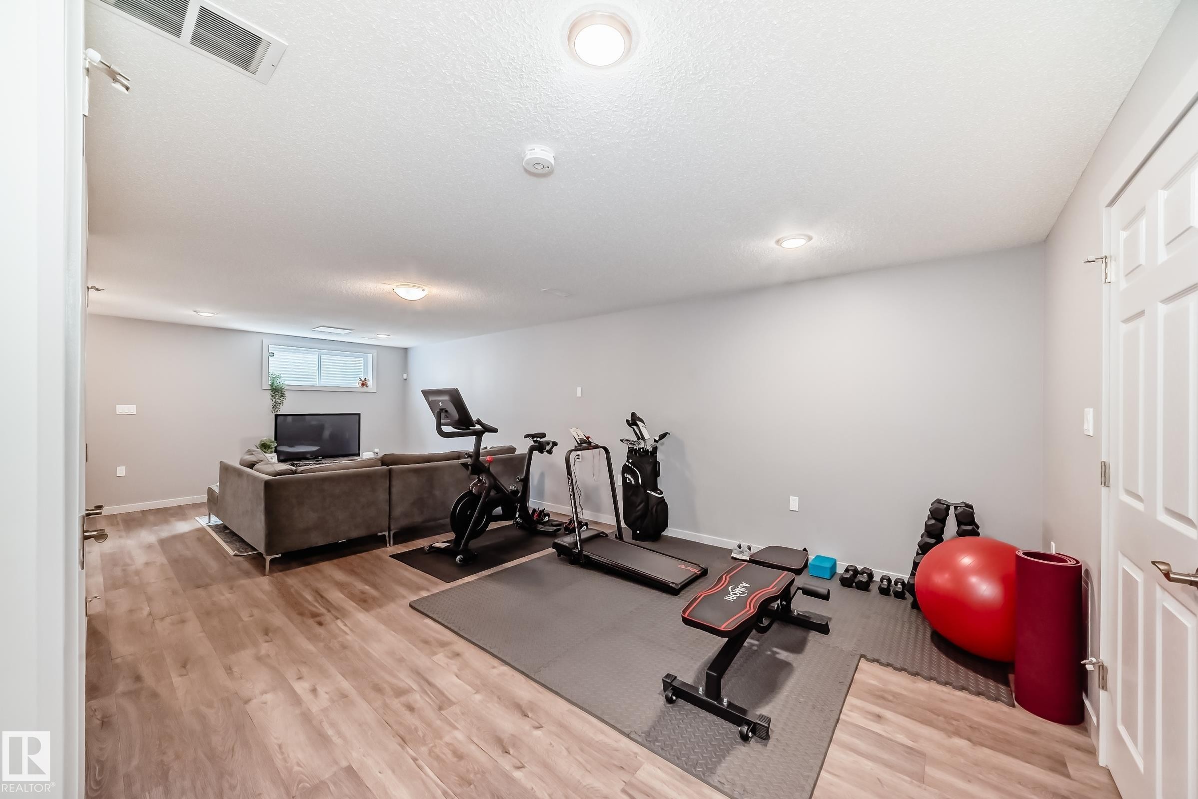 Finished lower level featuring recessed lighting, wood-finish flooring, light gray wall paint, and a white paneled door - 6919 Cardinal Wynd, Edmonton, AB - Indoor Photo Showing Gym Room