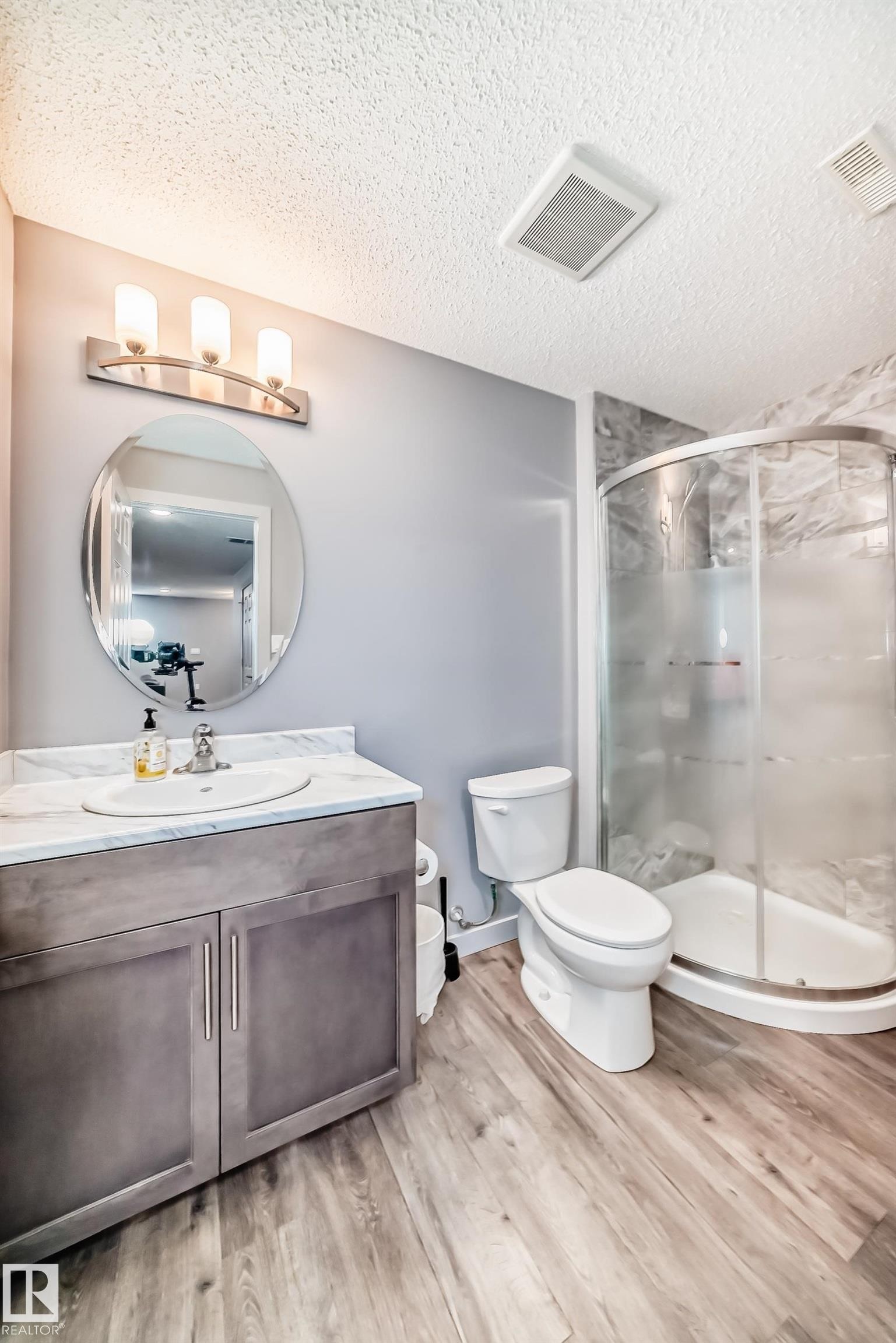Bathroom featuring a single vanity with a white countertop and undermount sink, brushed nickel hardware, and wood-finish flooring - 6919 Cardinal Wynd, Edmonton, AB - Indoor Photo Showing Bathroom