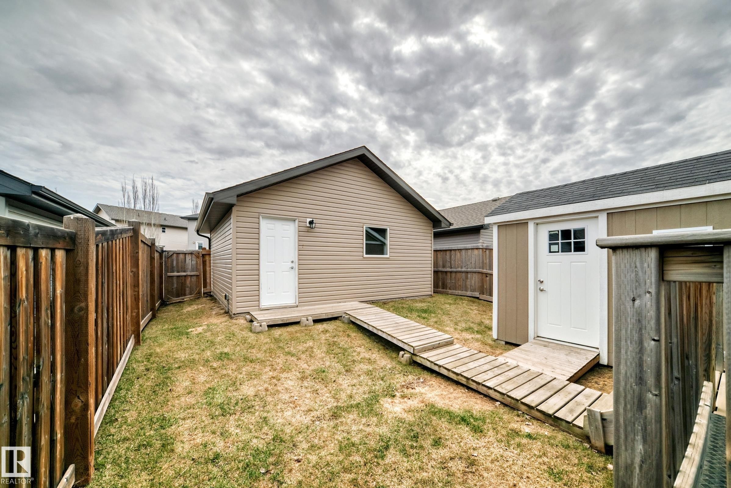 Fenced yard featuring two detached outbuildings with wood-finish ramps and perimeter fencing - 6919 Cardinal Wynd, Edmonton, AB - Outdoor With Exterior
