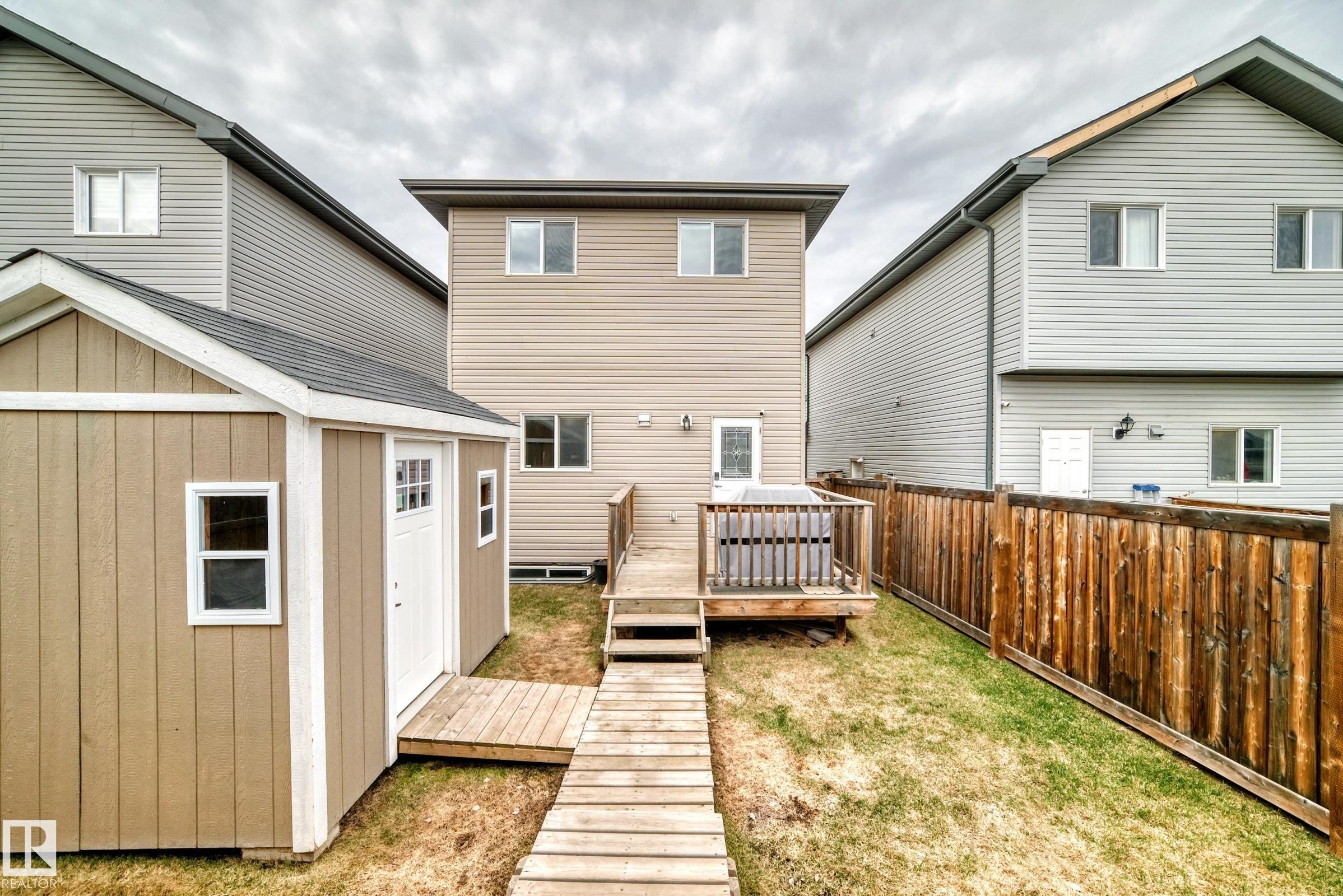Expansive backyard featuring a wood privacy fence, a 2 detached sheds with a white entry door and window, a wood-plank pathway - 6919 Cardinal Wynd, Edmonton, AB - Outdoor With Deck Patio Veranda With Exterior